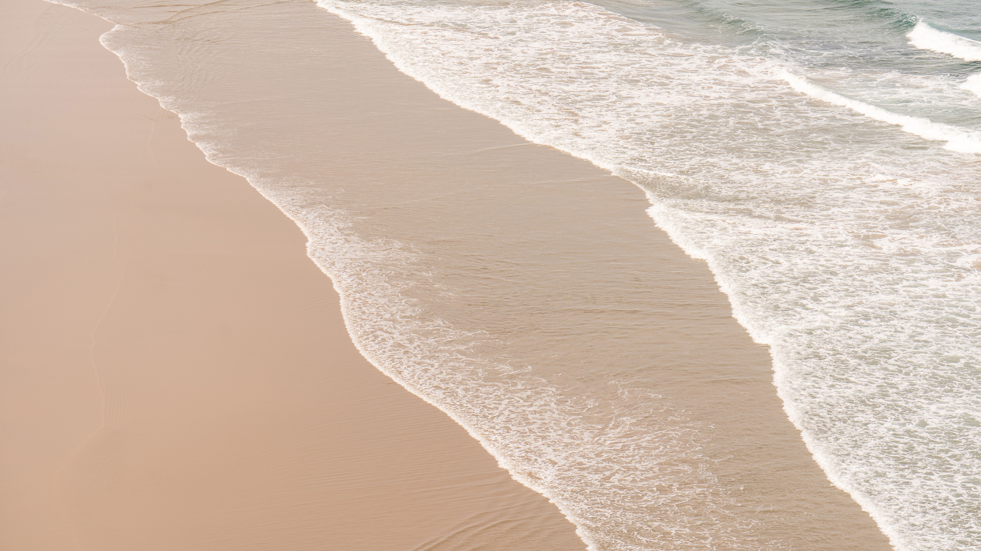 Aerial view of a sandy beach with waves gently crashing onto the shoreline.
