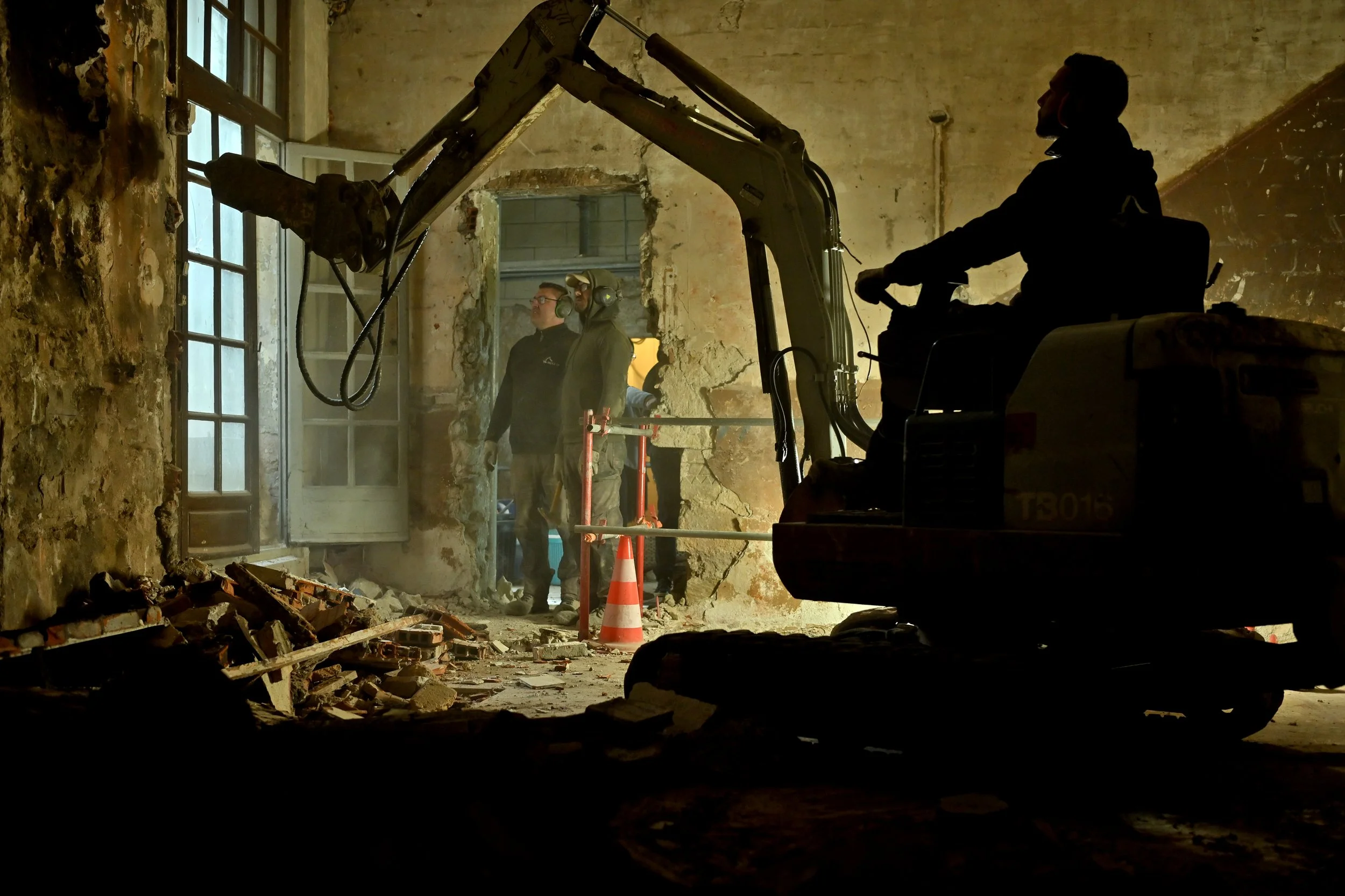 Travaux de démolition ou de rénovation dans un bâtiment ancien avec des ouvriers et une mini-pelle