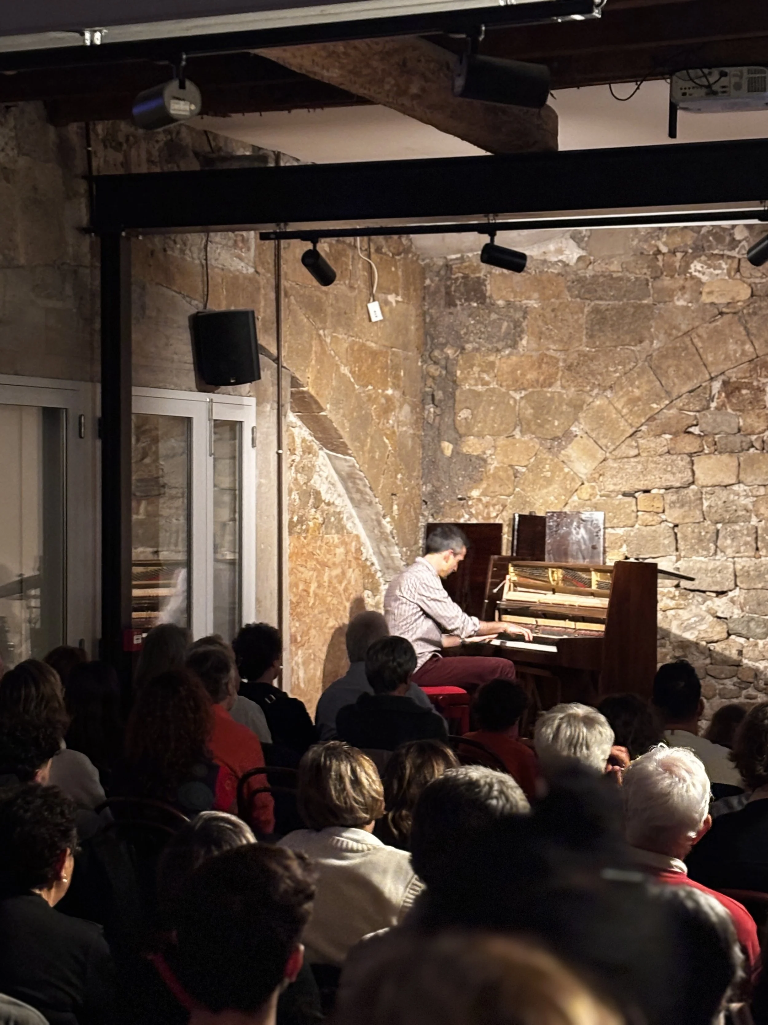 Un homme joue du piano devant un public dans une salle avec des murs en pierre.