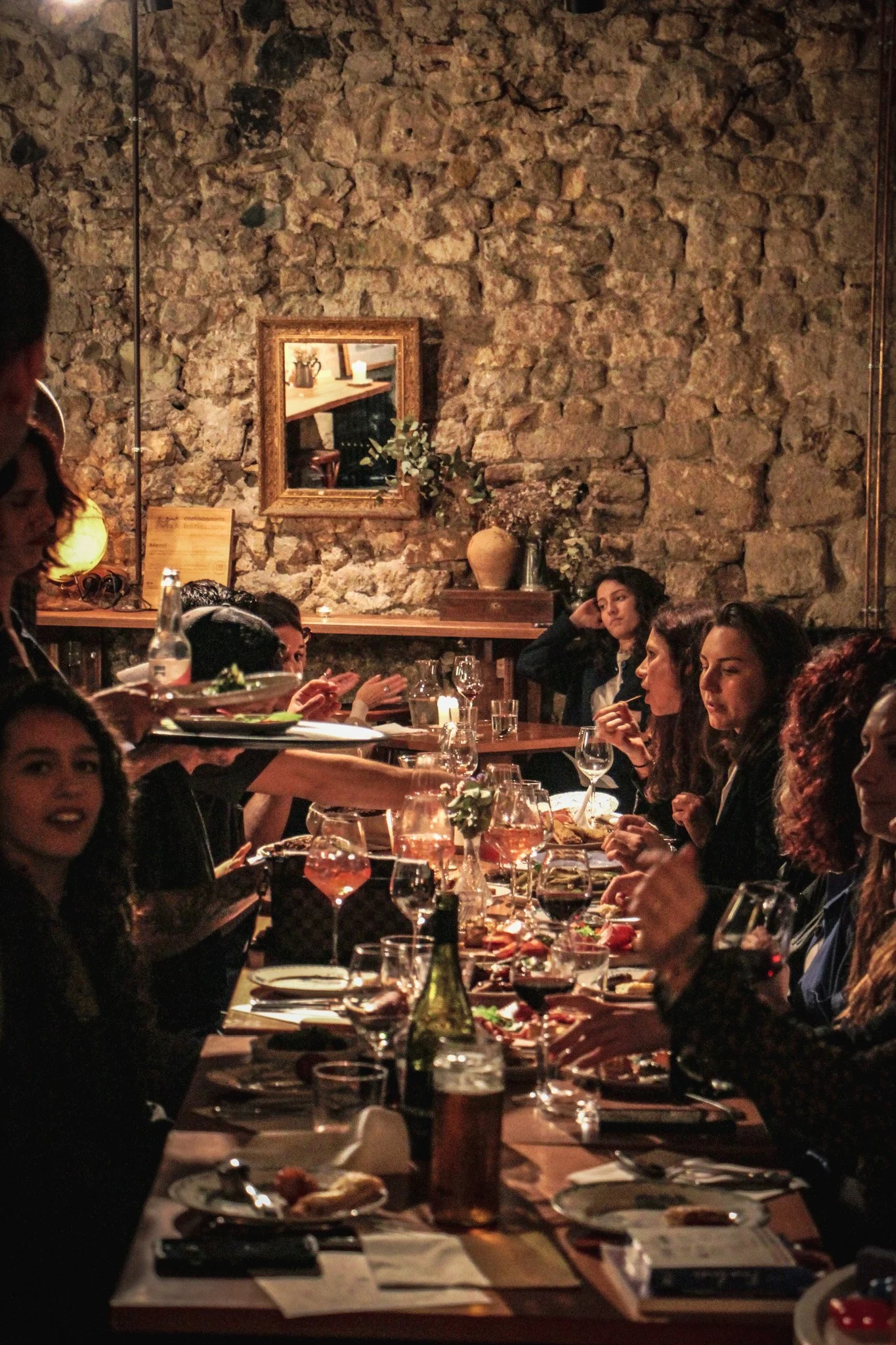 Groupe de personnes assises autour d'une table dans un restaurant avec un mur en pierre en arrière-plan, partageant un repas convivial.