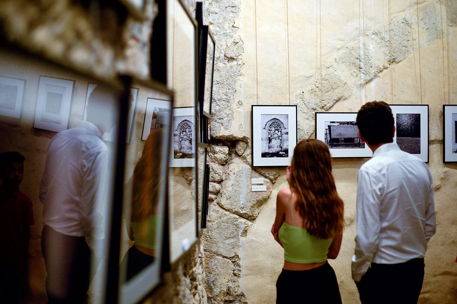 Deux personnes regardent une exposition de photos en noir et blanc dans une galerie avec un mur en pierre.