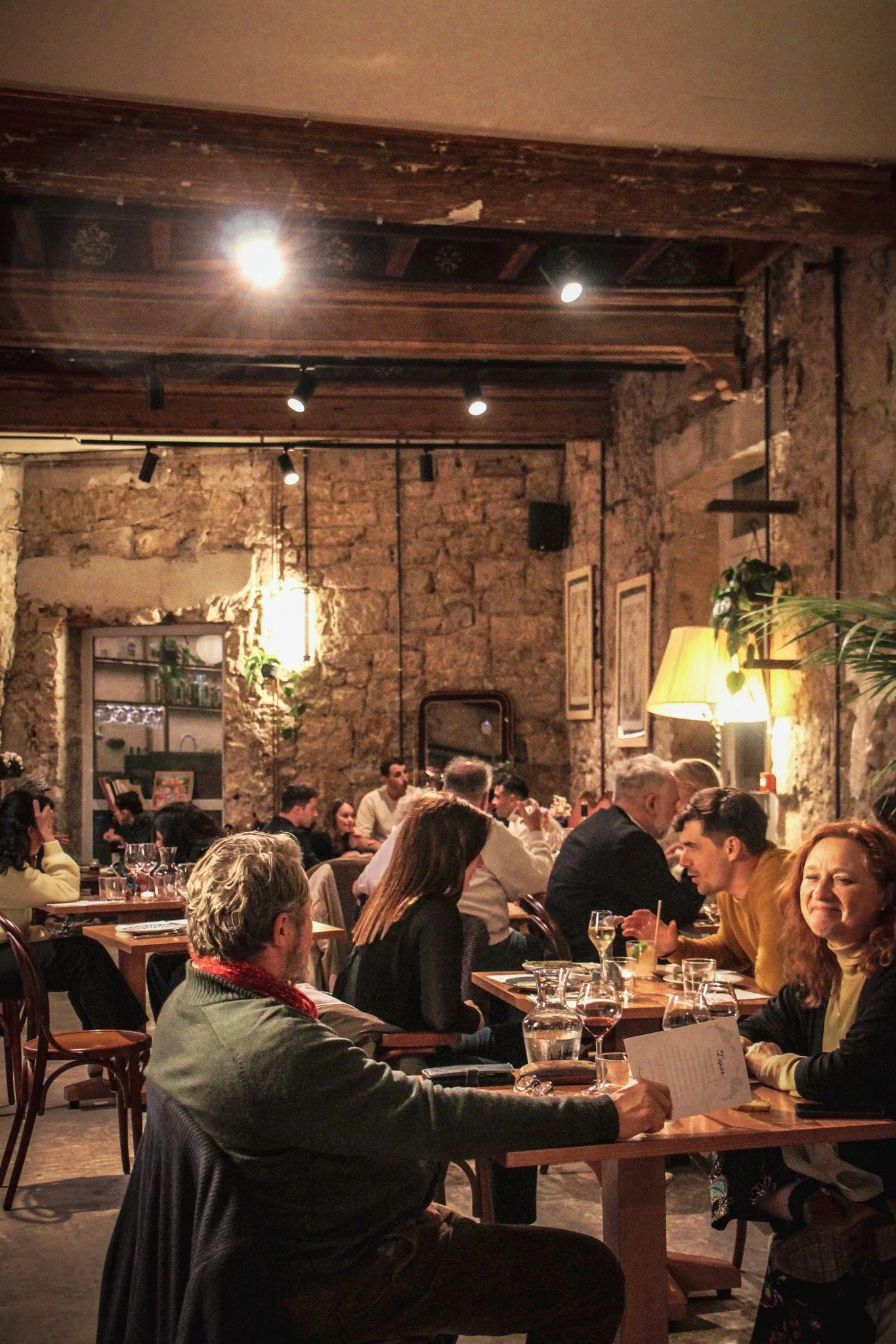 Un restaurant animé avec des personnes assises à des tables en bois, ambiance chaleureuse avec murs en pierre et éclairage tamisé.