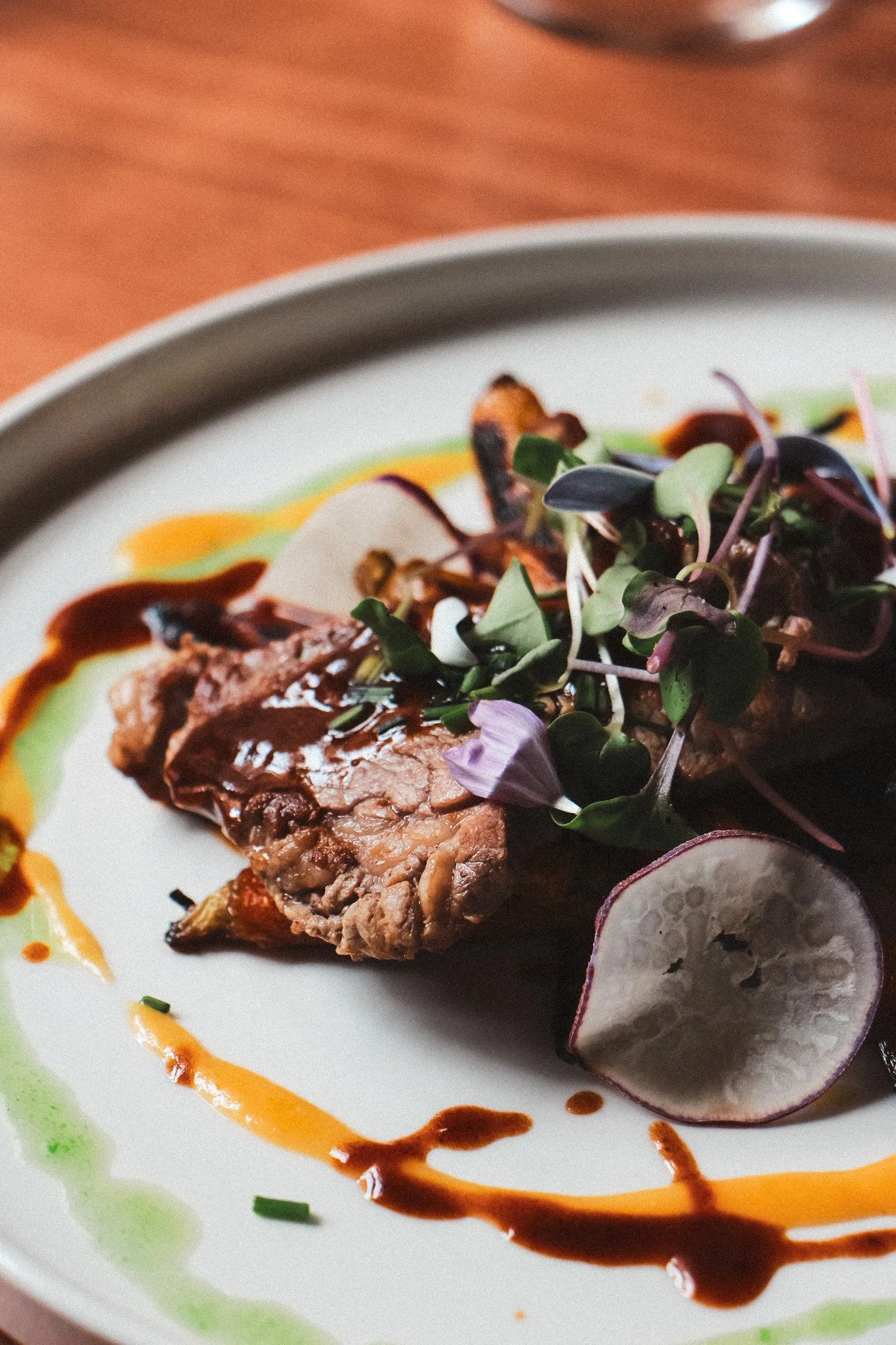 Assiette avec une portion de viande, des radis, des microgreens, et des sauces colorées.