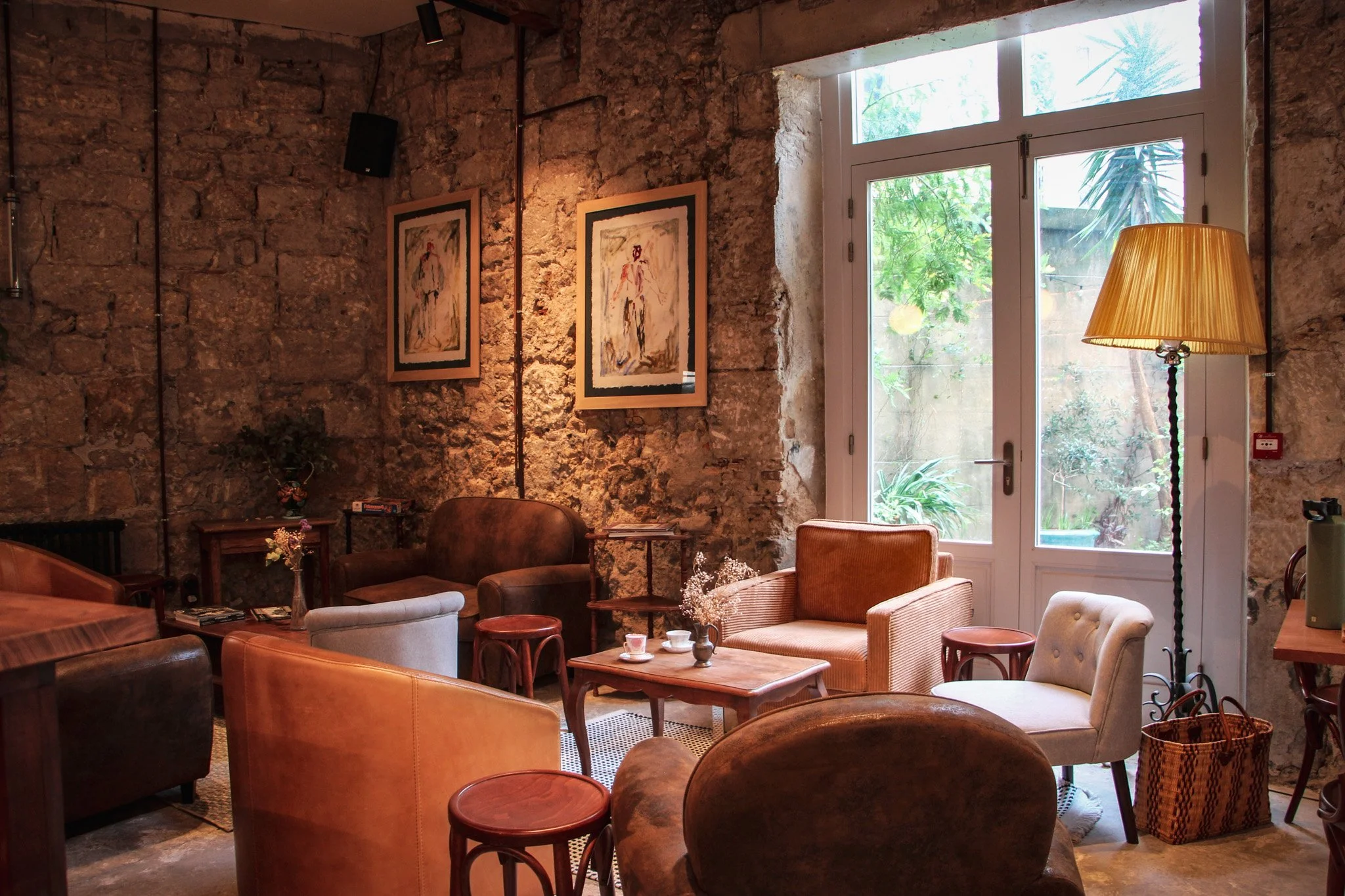 Un salon confortable avec des fauteuils en cuir, des petites tables en bois, un mur en pierre, une grande fenêtre laissant entrer la lumière naturelle et des œuvres d'art accrochées au mur.