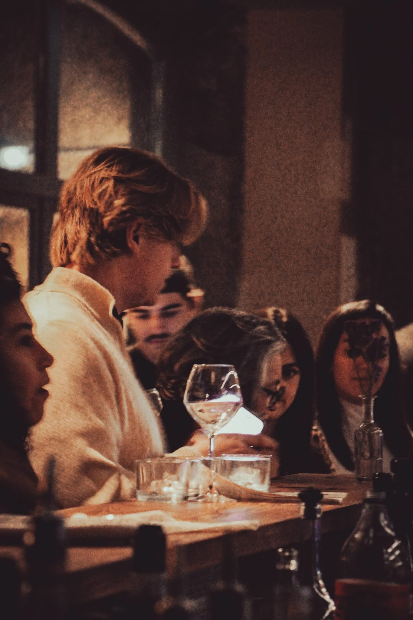 Un groupe de personnes assises autour d'une table avec des verres à vin, dans une ambiance chaleureuse et sombre.