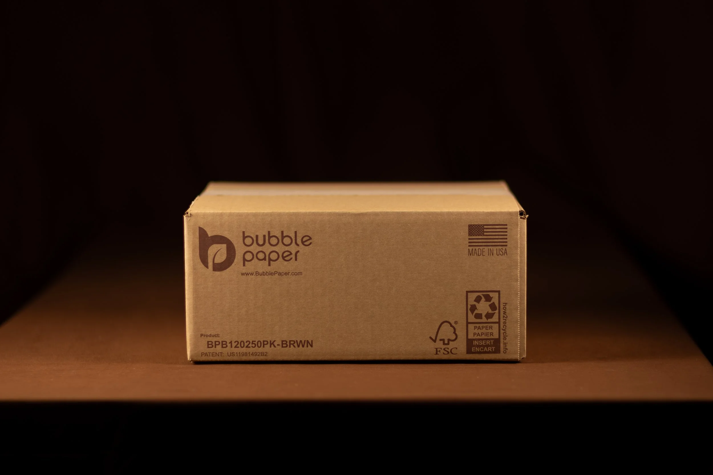 A cardboard box of bubble paper, labeled with recycling symbols and product details, placed on a dark surface with a black background.