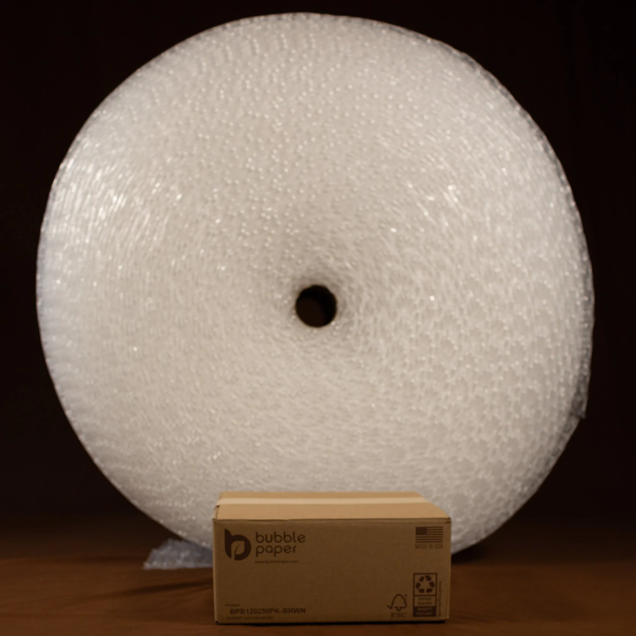 A round bubble lamp with a white, textured, semi-opaque surface is illuminated from within, casting soft light in a dark room. It is placed on a wooden surface, with a cardboard box labeled 'bubble paper' underneath.