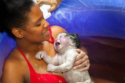 Woman holding a newborn baby during a water birth in a birthing pool