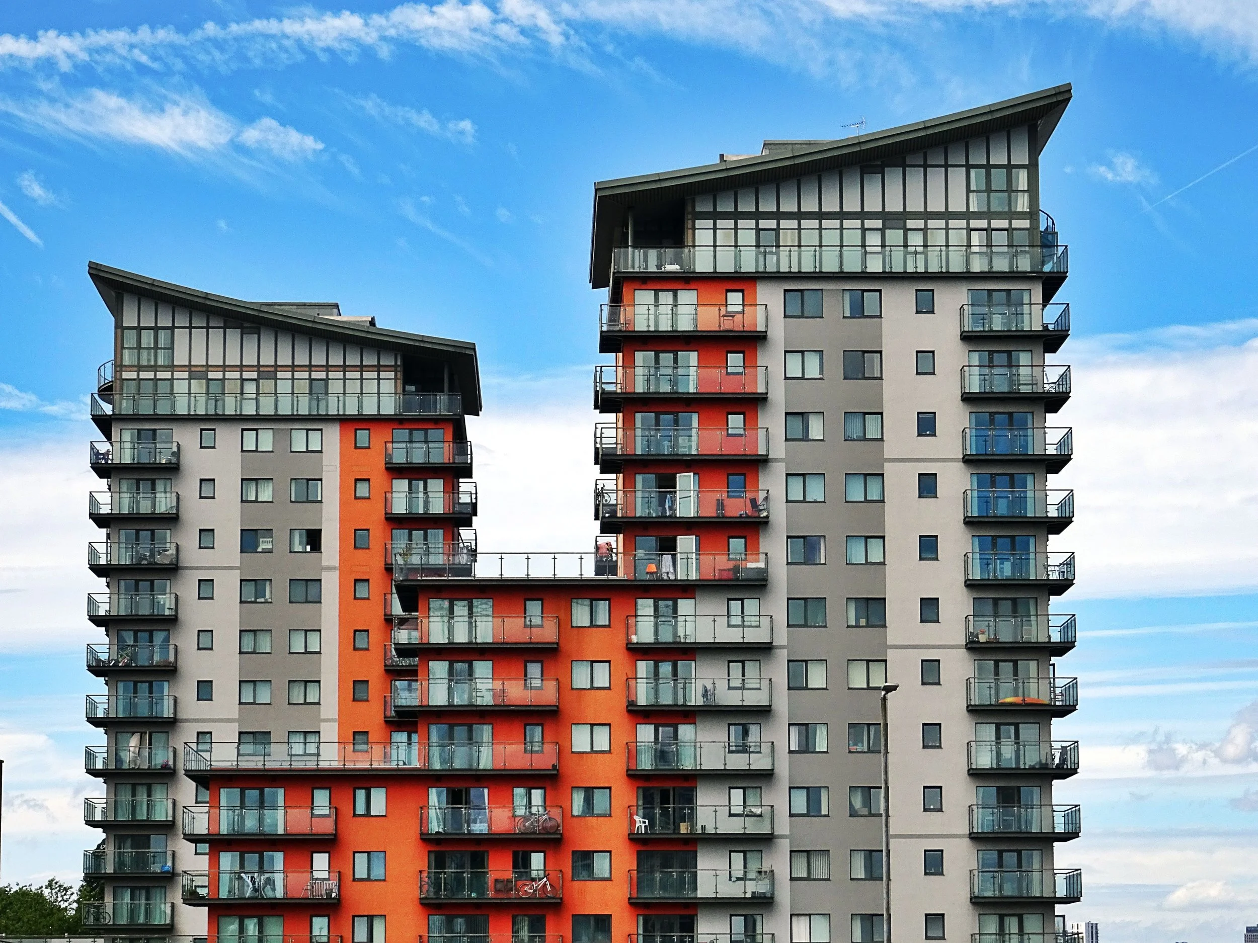 Modern multi-story apartment buildings with glass balconies under a partly cloudy sky.