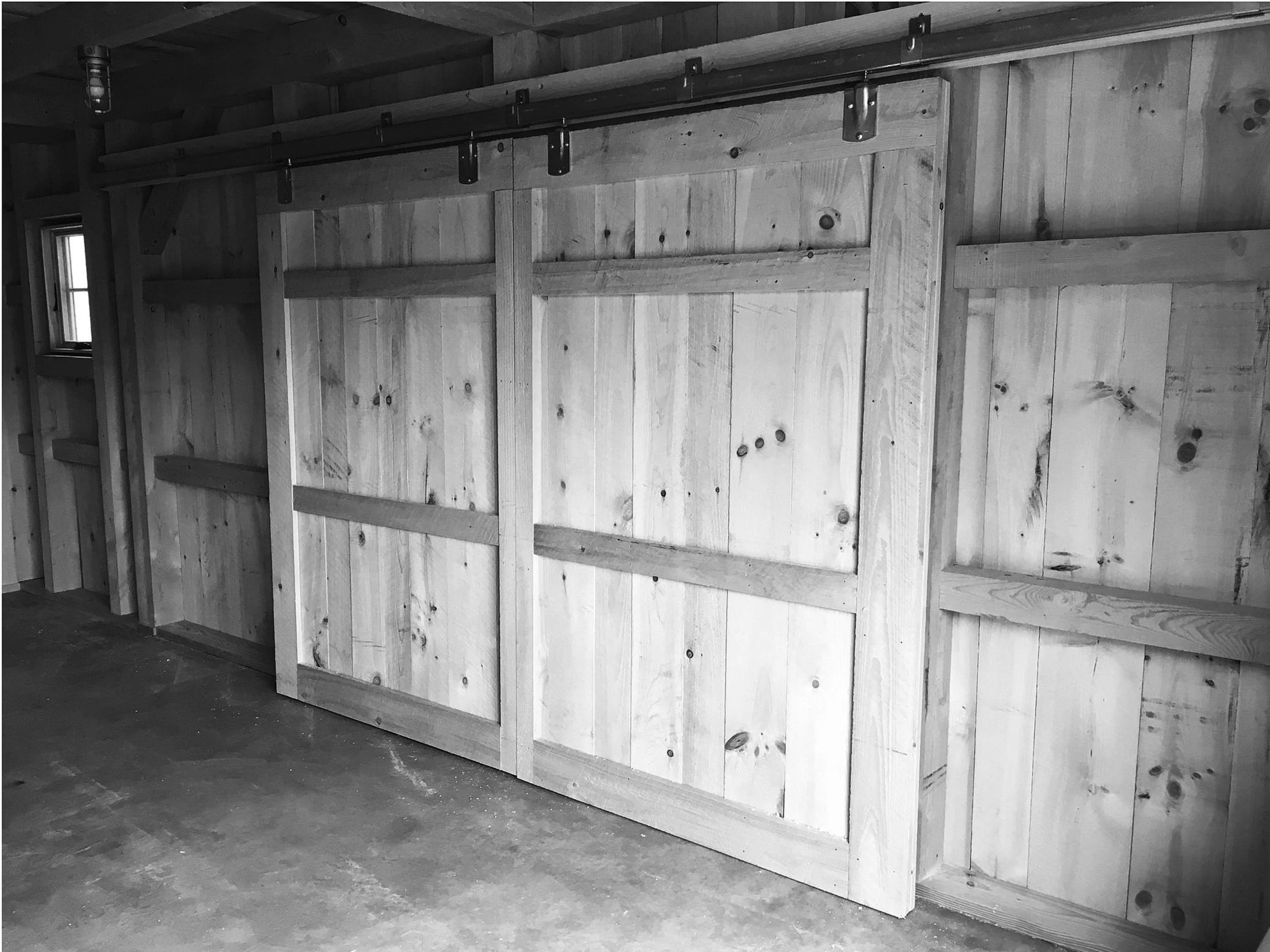 Interior of a wooden garage with a sliding barn door on a rail. Built by Timber, Stone, & Steel, lead contractor Taylor Prouty in Vermont.