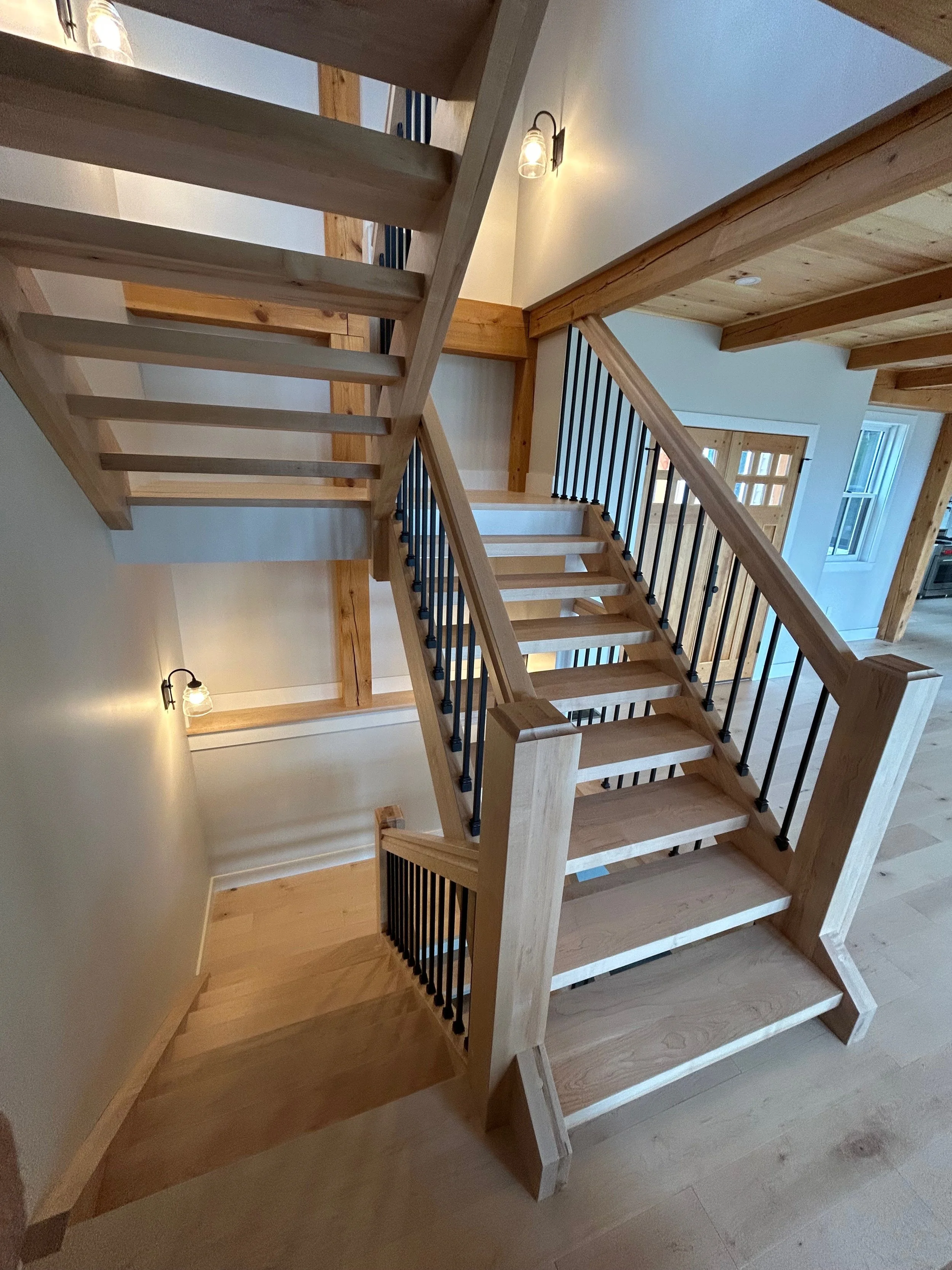 Wooden staircase inside a house with black metal railing and wooden beams. Built by the Timber, Stone, & Steel lead contractor, Taylor Prouty, in Vermont.