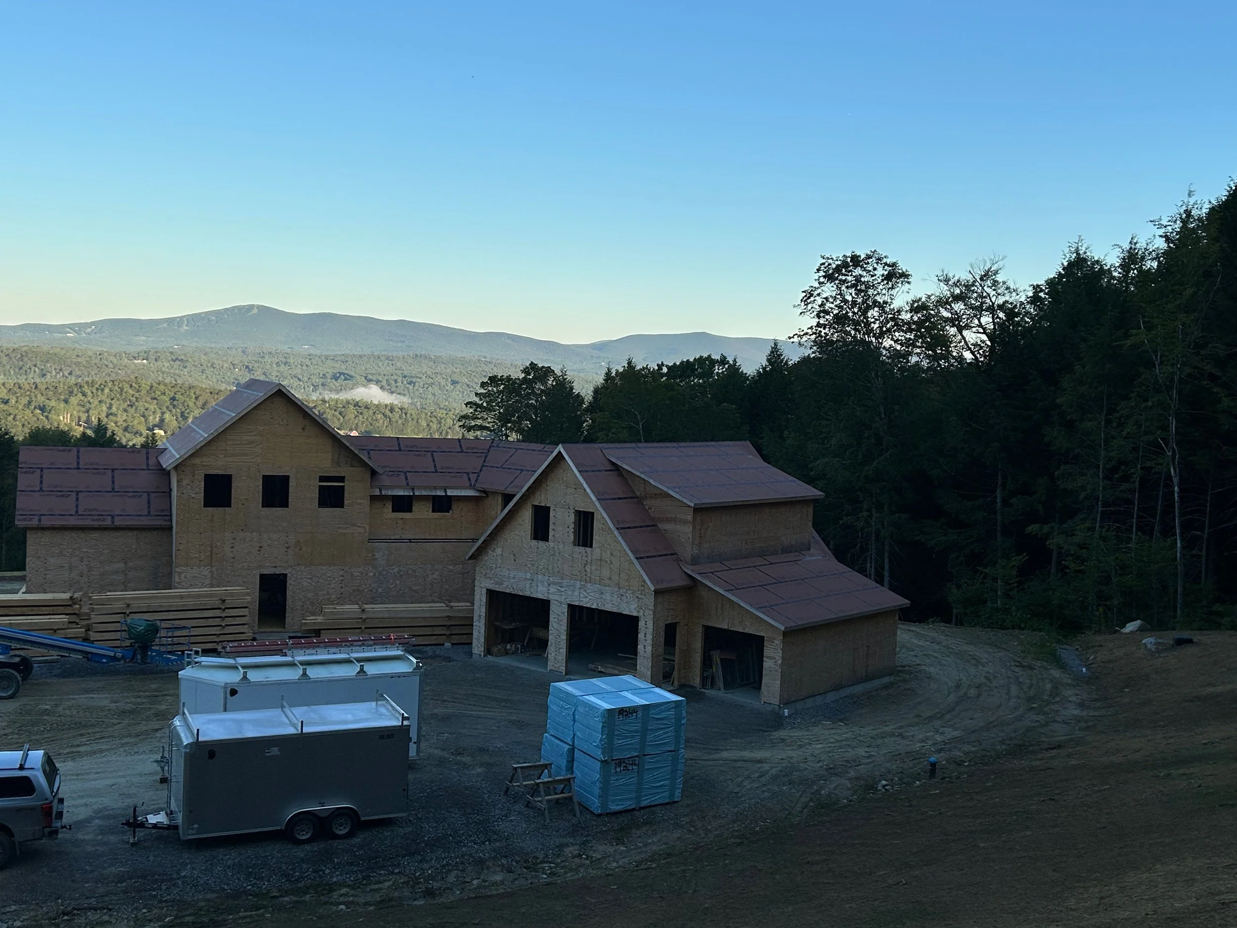 Under construction wooden house on a hill with mountain and forest background. Built by the Timber, Stone, & Steel lead contractor, Taylor Prouty, in Vermont.