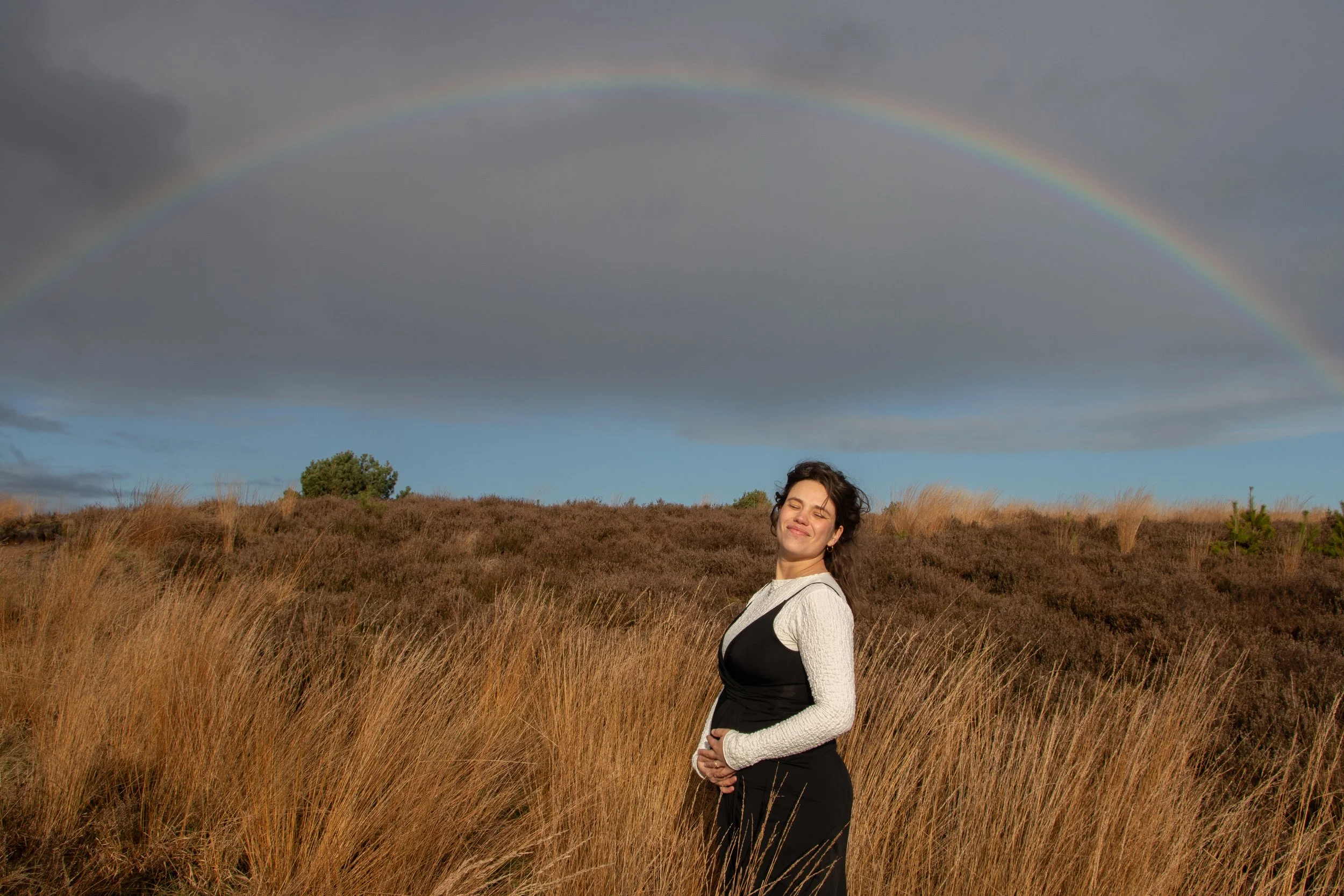 Zwangerschaps fotoshoot in het open veld met een regenboog.