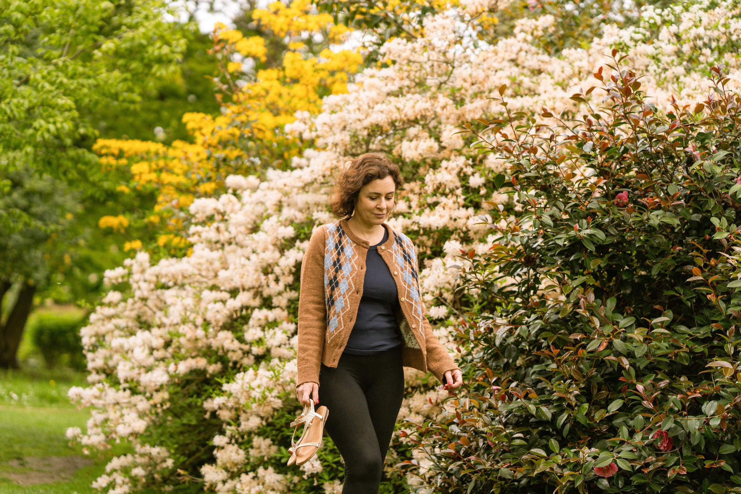 A woman walking on a path surrounded by blooming flowers and trees in spring or summer.