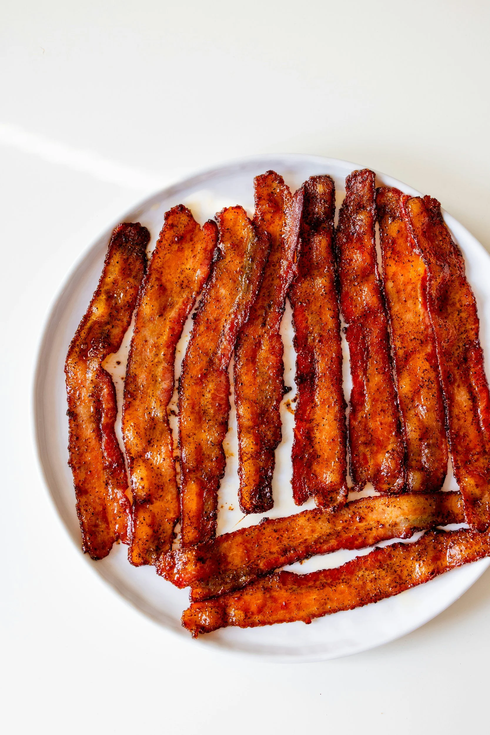 Bacon strips on a white plate with a white background.