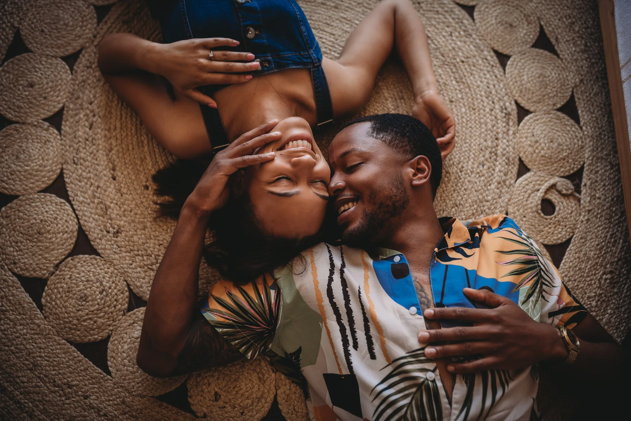 Couple lying on a woven rug, smiling and embracing each other.