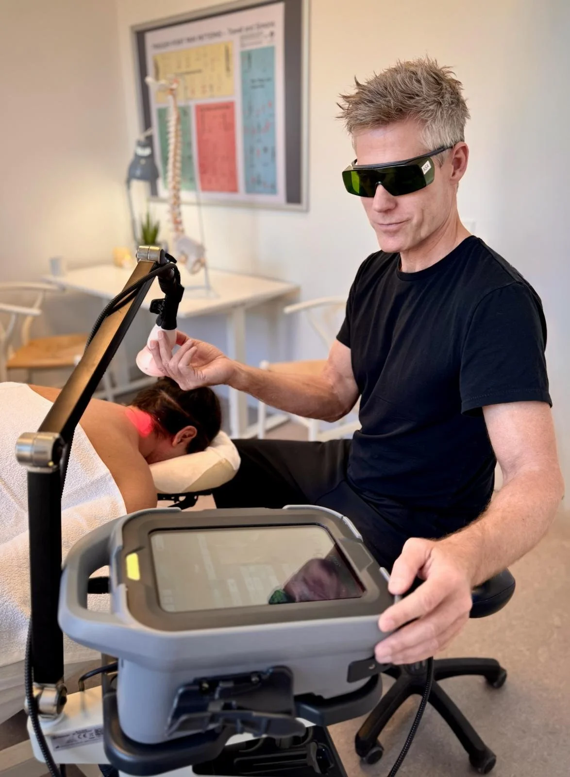 Behandler med beskyttelsesbriller udfører laserterapi på patient i klinik, hvor ASAlaser medicinsk laserudstyr anvendes til målrettet MLS-laserbehandling.