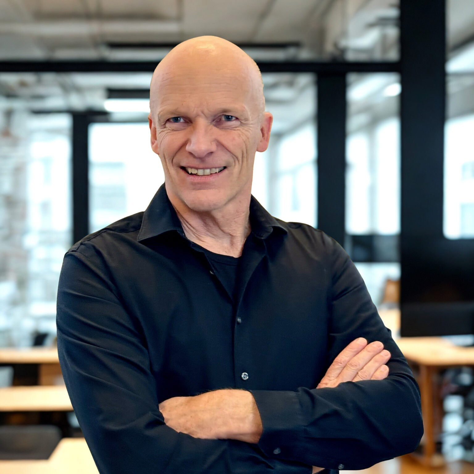 Mand i sort skjorte, skaldet og står med armene over kors og smiler - New Yorker glasrude baggrund, Bo Simonsen