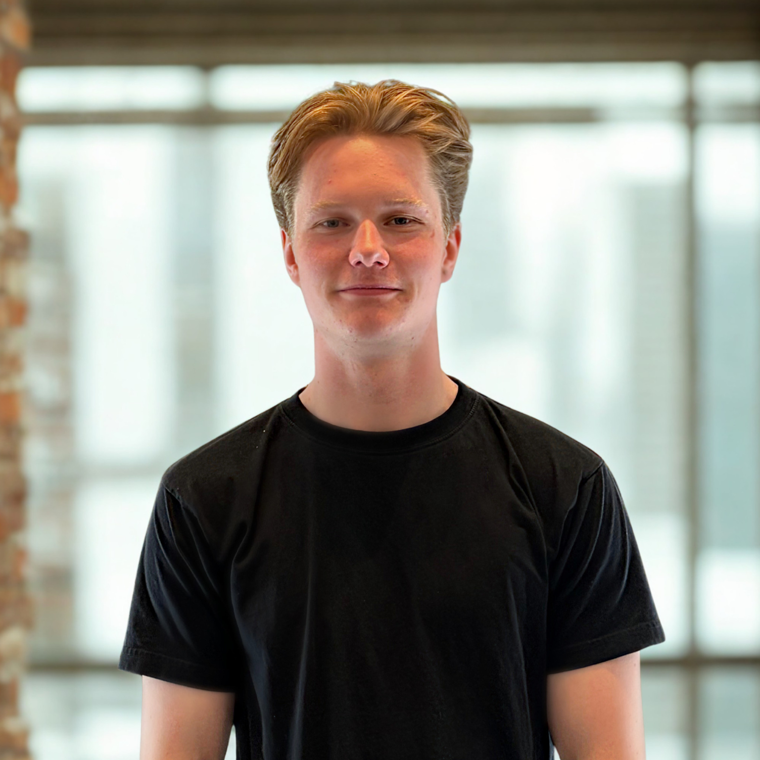Yngre mand med sort t-shirt og mellemblondt hår, New Yorker glasrude baggrund - Mathias Tryde
