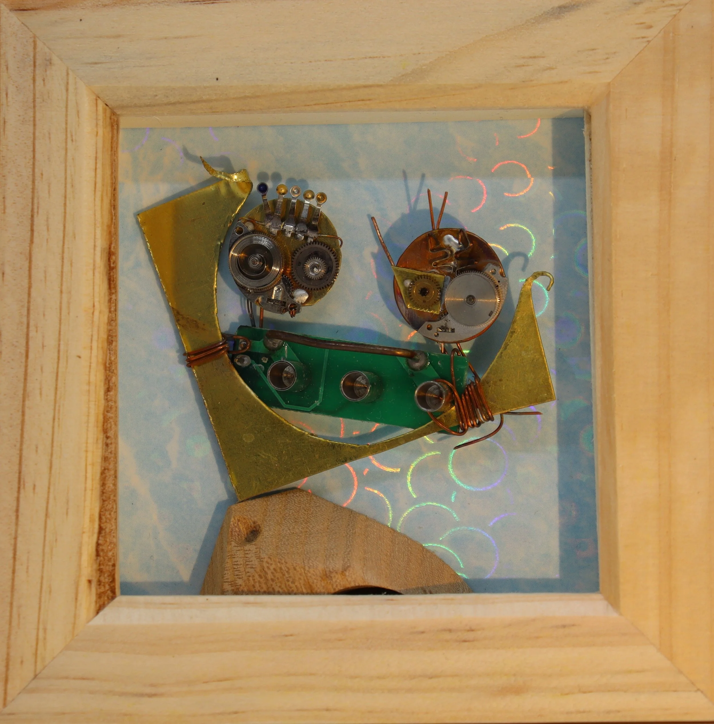 A framed mechanical art piece resembling a dragonfly, made from various metal watch parts and gears, with a background featuring colorful holographic circles.