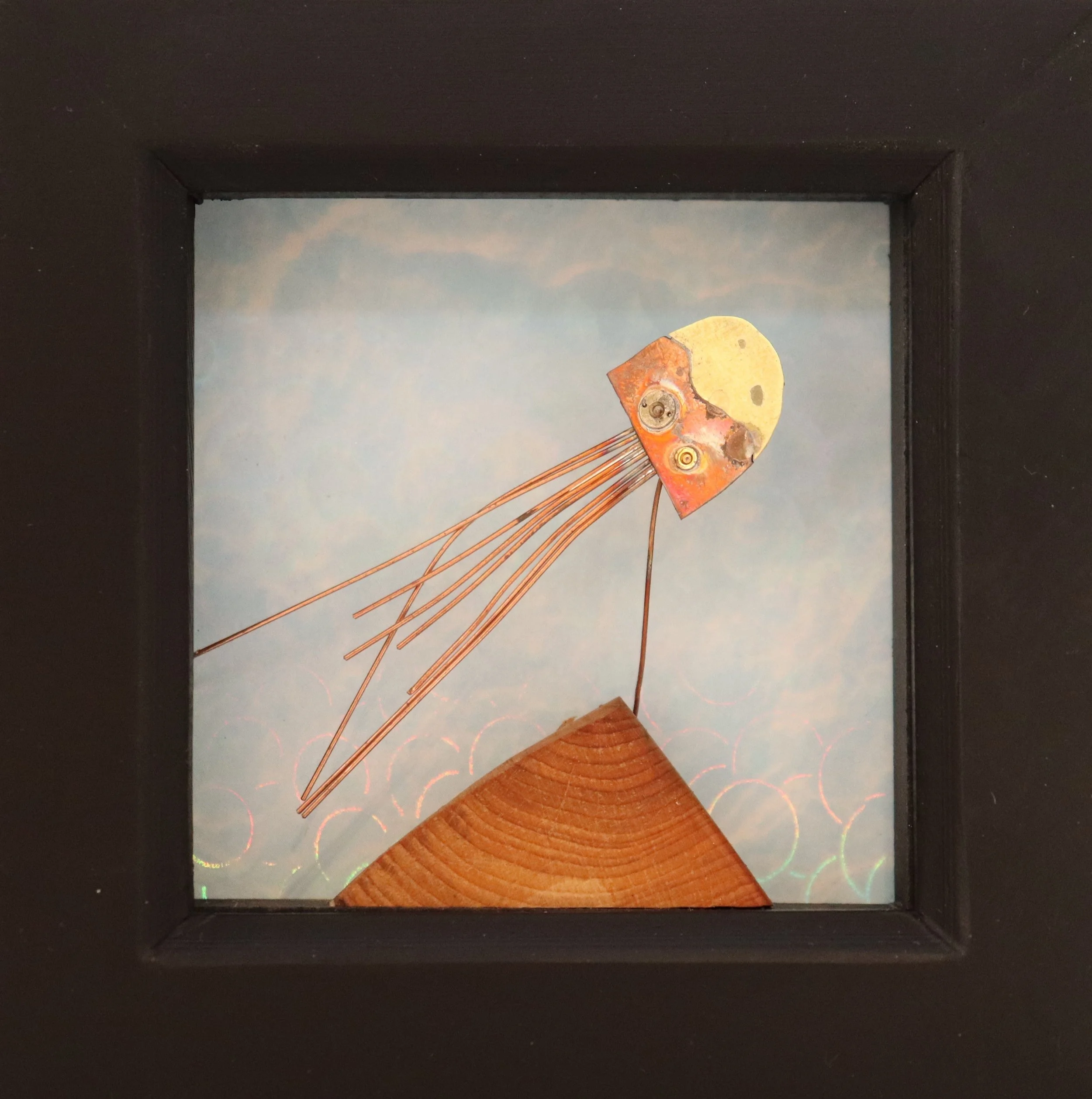 Mixed media art piece featuring a moon and a fish with elongated fins, mounted on a wood piece, displayed in a black frame with a light blue sky background.