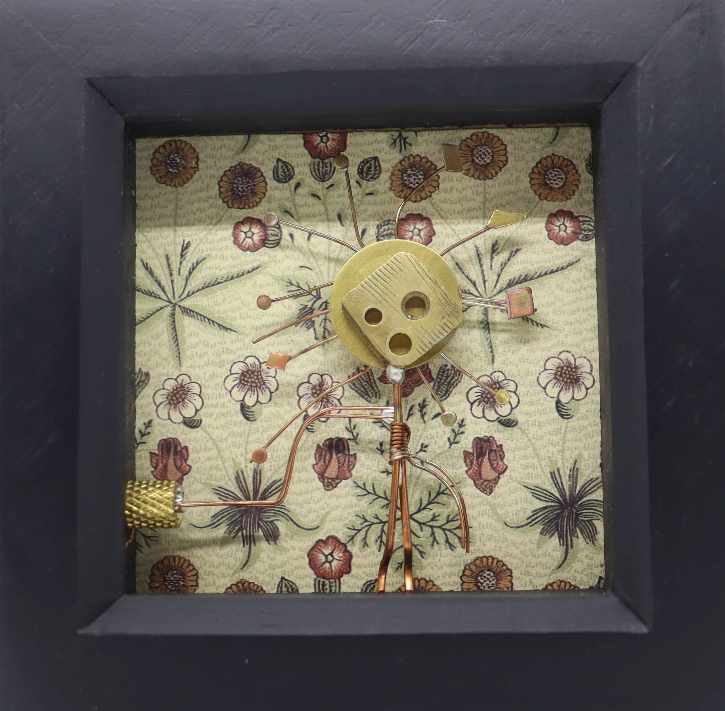 A decorative clock with a floral background, featuring a brass face with holes, surrounded by thin metal rods with leaves and geometric shapes at the ends, all set inside a black frame.