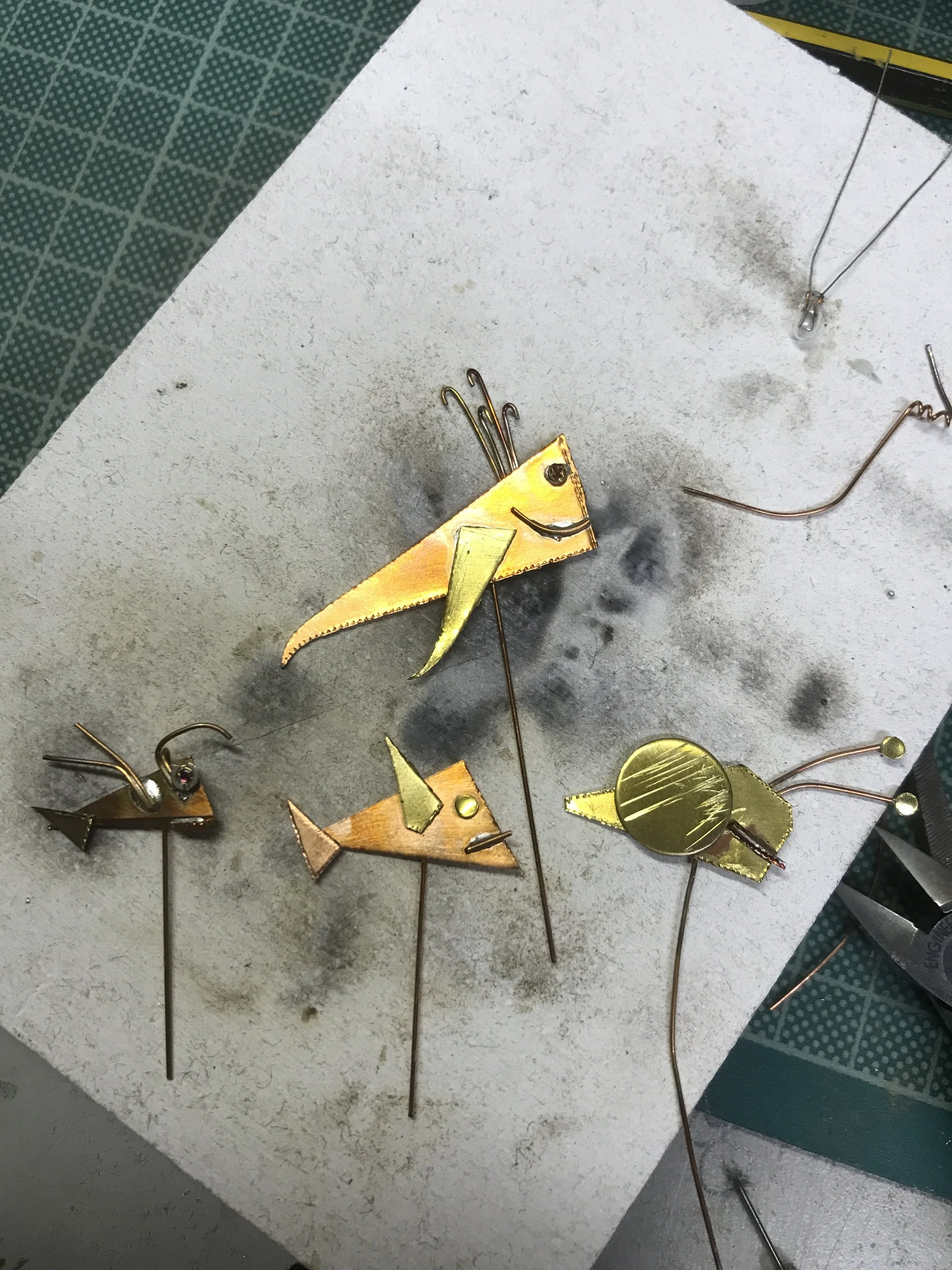 Several small metal art sculptures resembling fish with colorful bodies and exaggerated features on a white work surface.