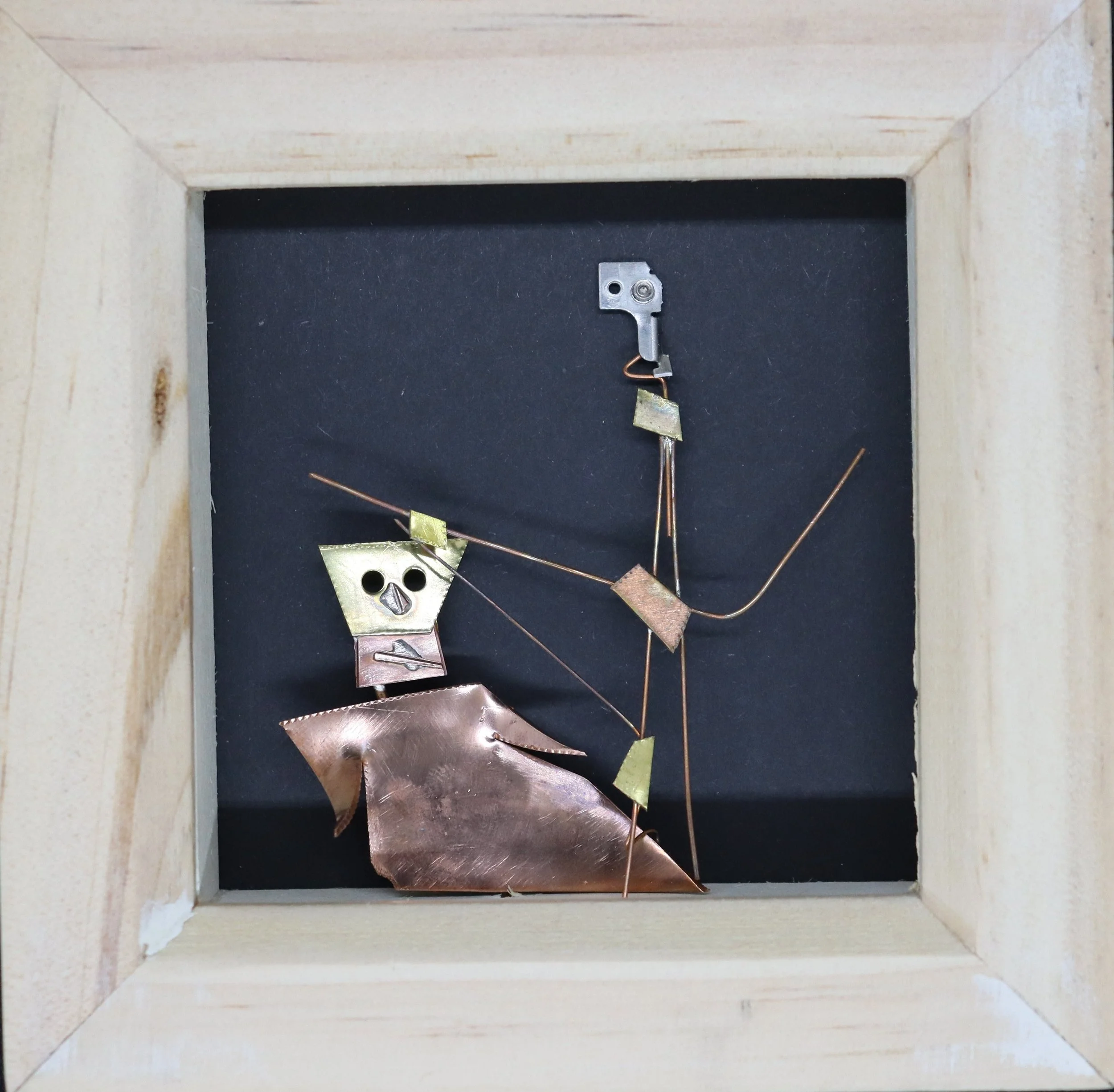 A metallic sculpture of a human figure riding a horse inside a wooden frame