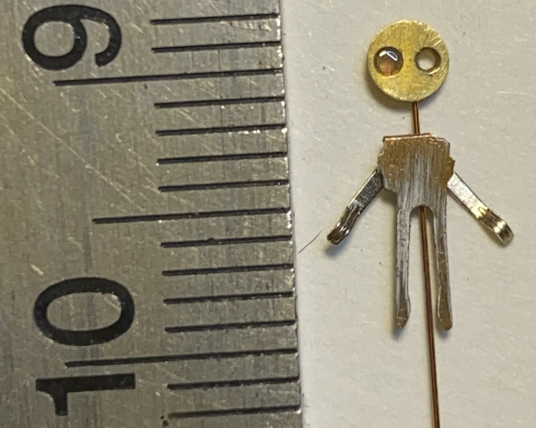 Small humanoid robot made of metallic parts next to a ruler for scale.