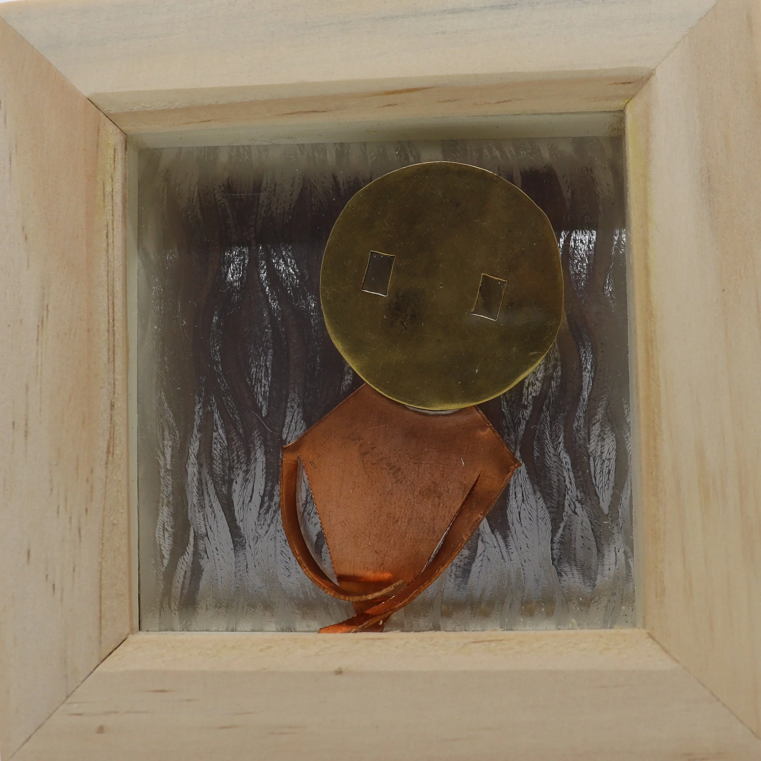 A handmade robot figure made from a circular metallic disk for a face, a copper-colored metallic piece for the body, and a brown leather strap for a neck, inside a wooden box with a reflective interior.