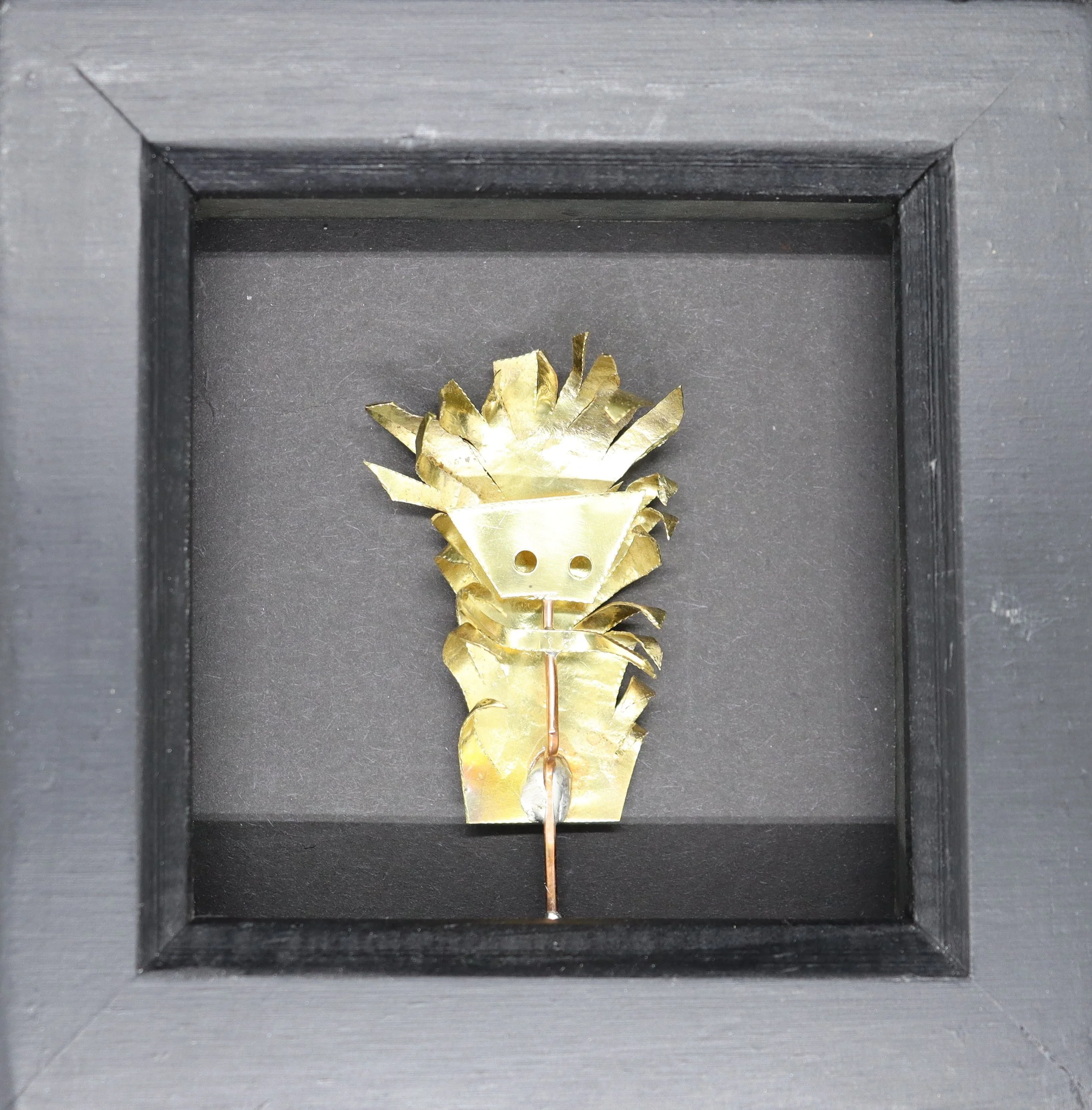 A small decorative pineapple made of gold-colored metal inside a black display case.