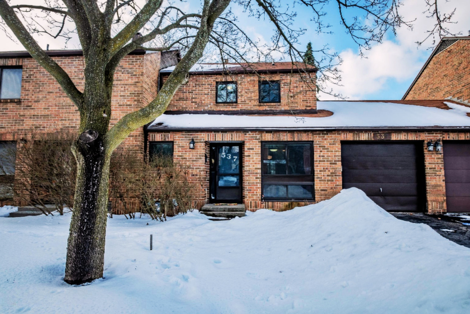 A brick house with a snow-covered yard, leafless trees, and a partially snow-covered roof during winter.