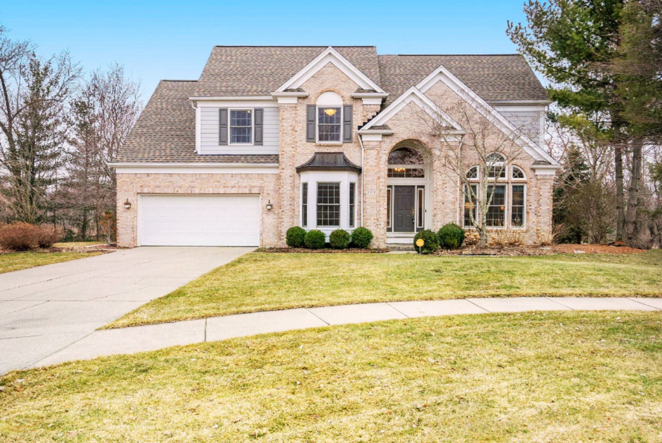 A two-story suburban house with brick and siding exterior, a front yard with grass, a driveway leading to a two-car garage, and a sidewalk in front.
