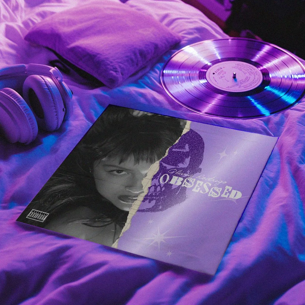 Vinyl record, headphones, and an album cover titled "Obsessed" with a woman's face on a purple bed, illuminated by purple and blue lighting.