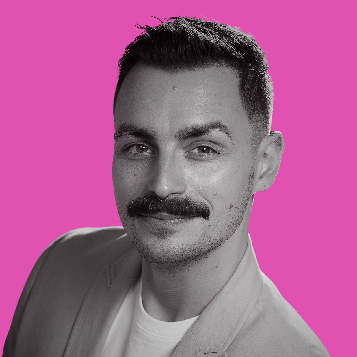 Black and white portrait of a man with a mustache and short styled hair, wearing a blazer and white shirt, against a pink background.