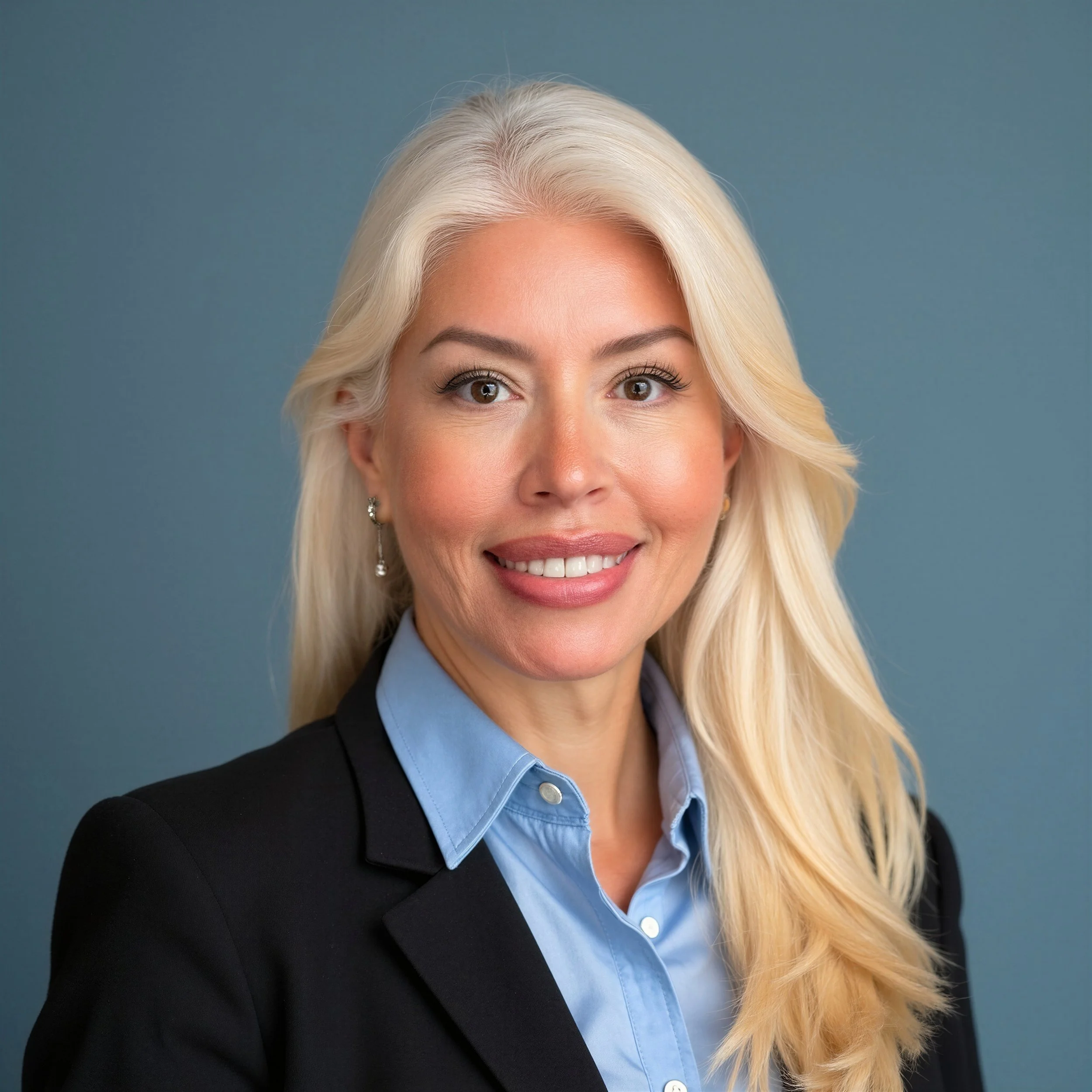 Close-up of a smiling woman with long blonde hair, wearing a black blazer and light blue collared shirt, against a plain blue background.