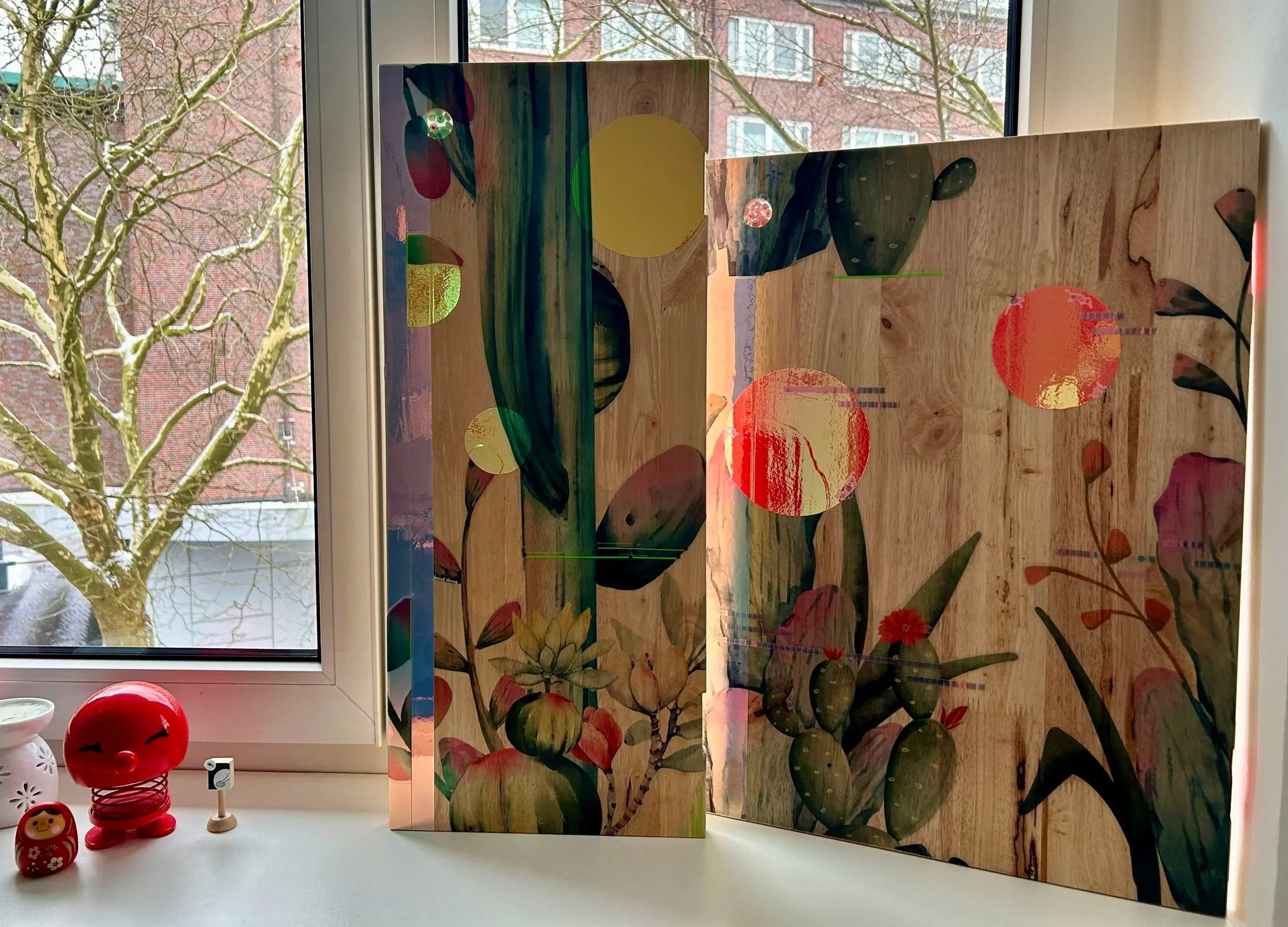 Decorative panels with botanical artwork set on a windowsill, with little cutouts where the daylight shines through.