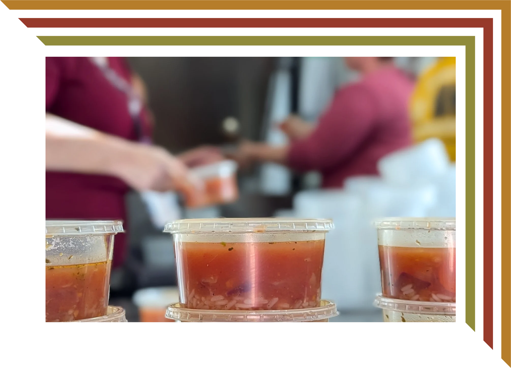 Containers of soup in the foreground with people serving food in the background.
