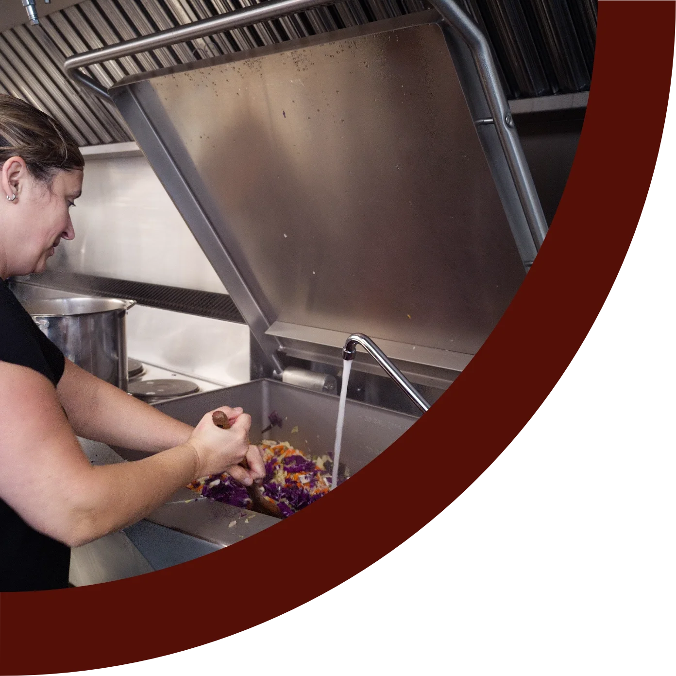 A woman washing colorful dishes in a commercial kitchen sink with running water.