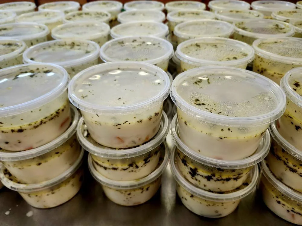 Multiple small plastic containers filled with a cream-based soup, stacked in rows.