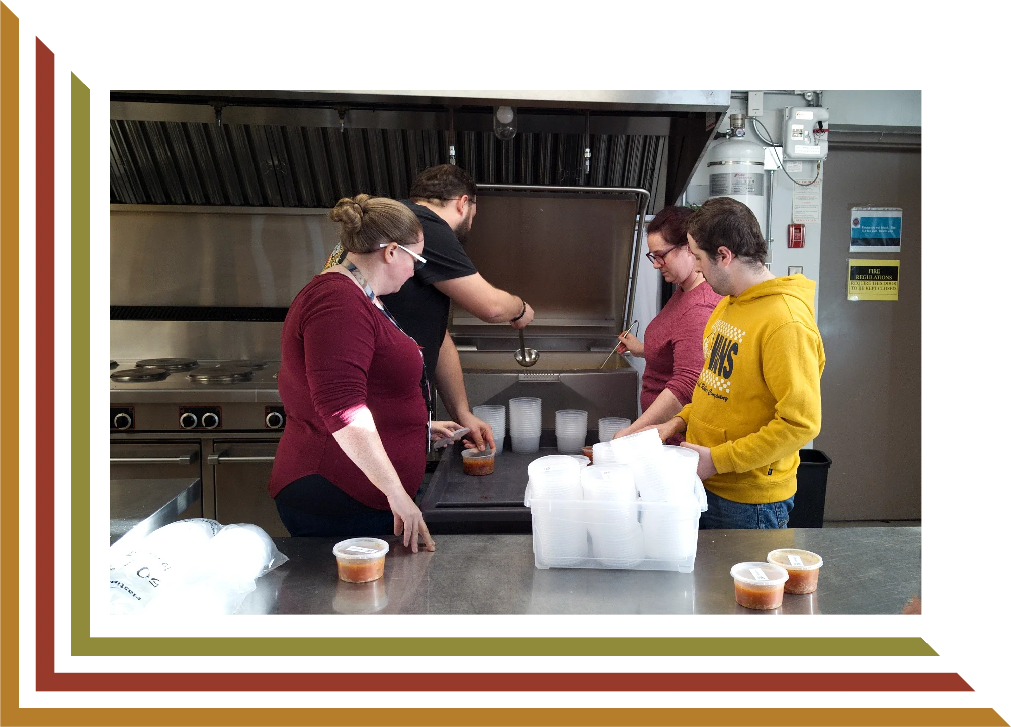 Group of four people packing containers of soup in a commercial kitchen.