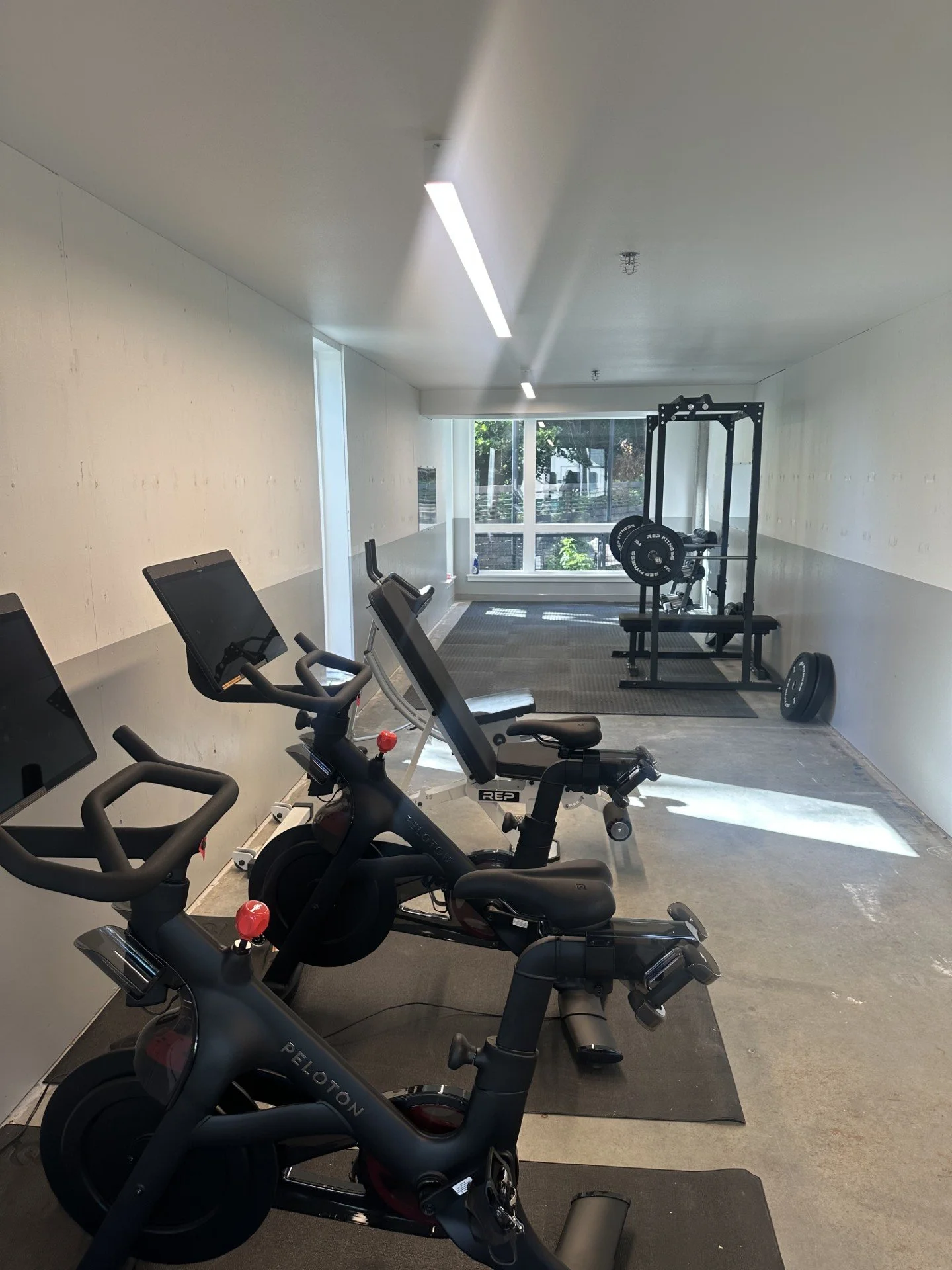 Community fitness center available to all residents, featuring Peloton equipment with complimentary in unit subscription, a weight bench, free weights, and dedicated open space for yoga and stretching.