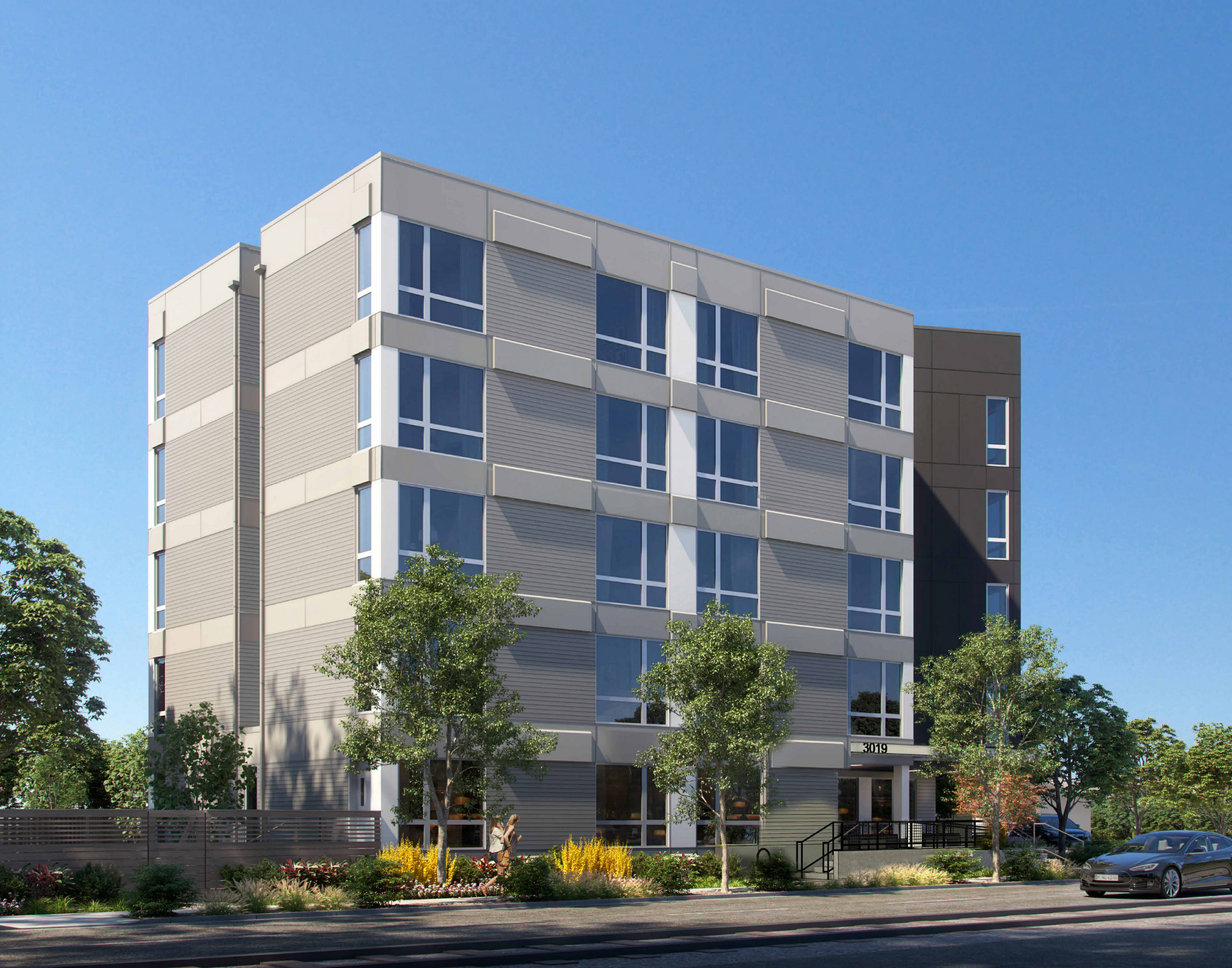 Modern apartment building with large windows and trees in the foreground under a clear blue sky.