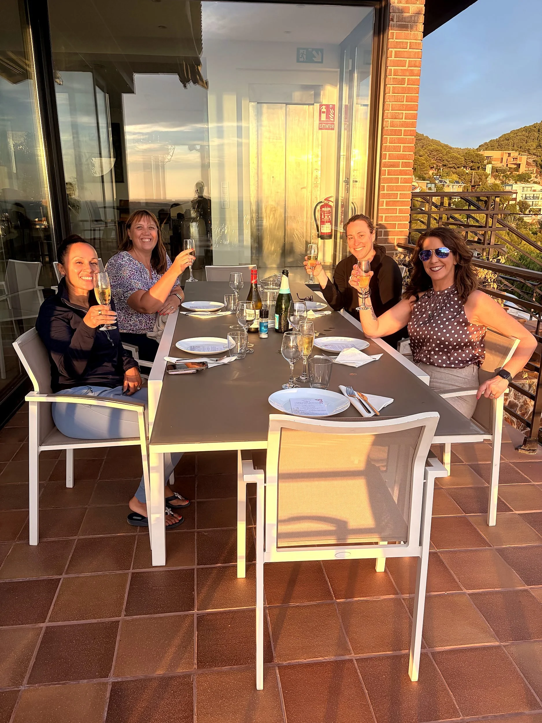 Women raising glasses at a long table on a villa terrace in golden evening light, Sitges