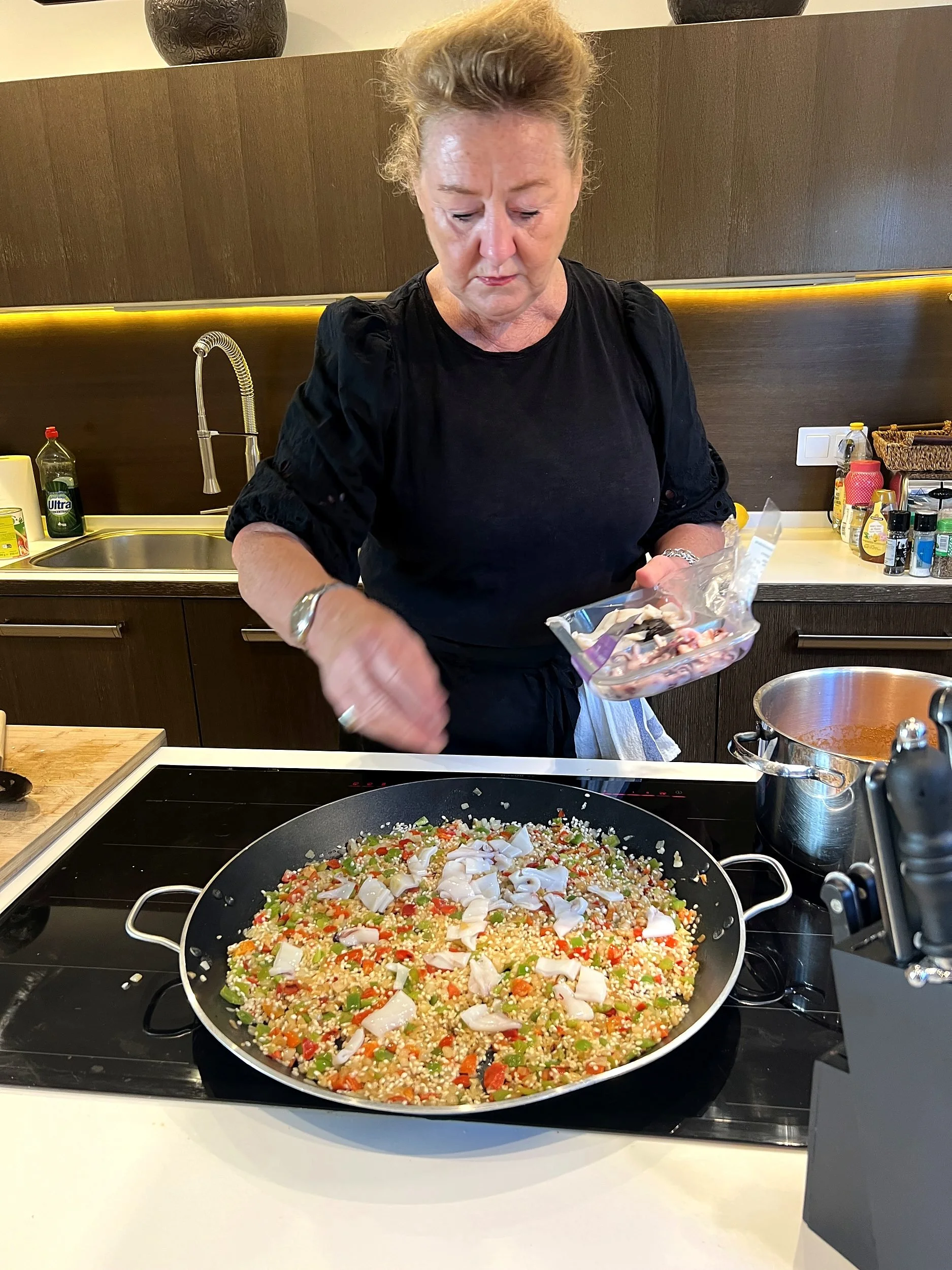 Chef Amanda adding seafood to a pan of paella in a villa kitchen in Sitges