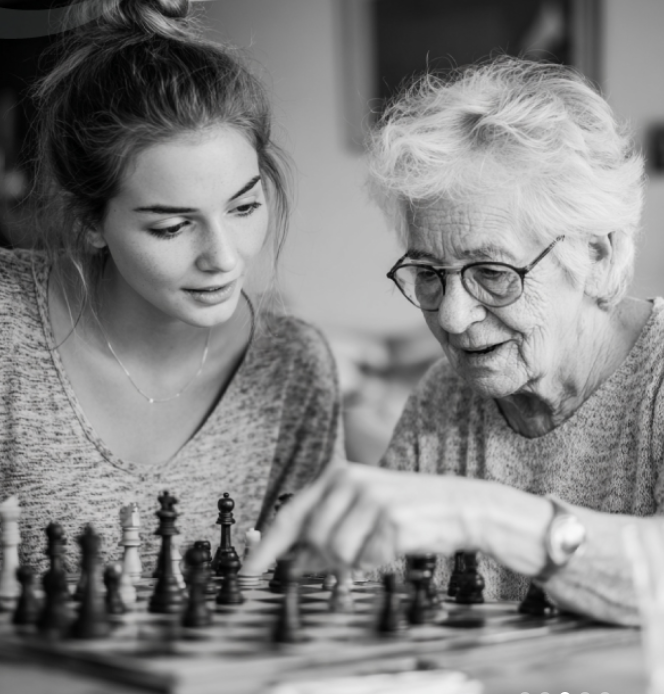 An elderly woman and a young woman playing chess together indoors.