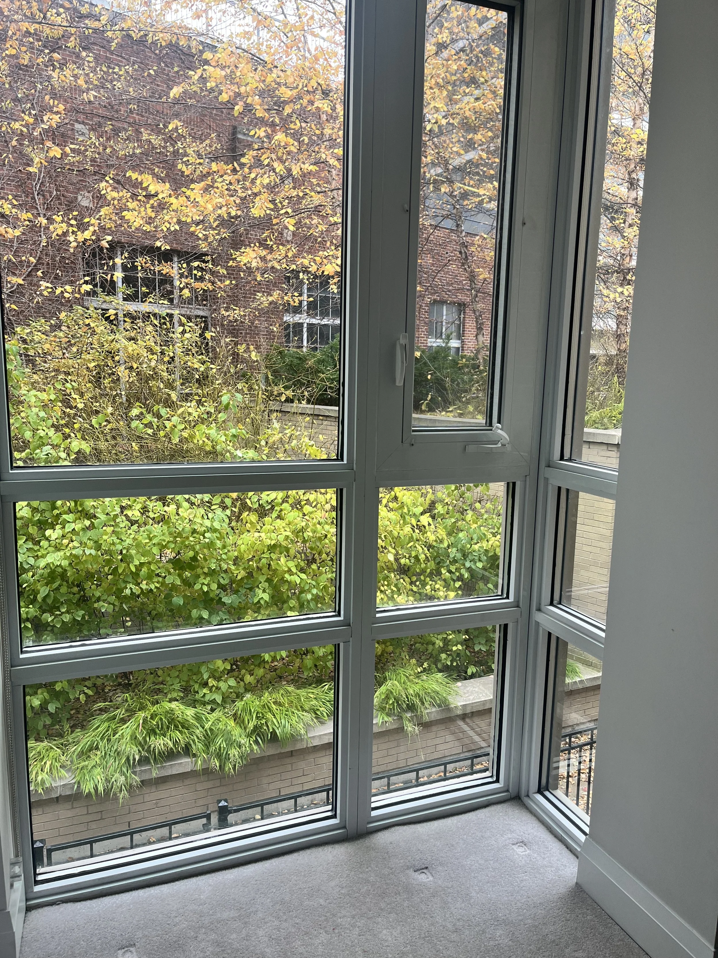 View of autumn trees and a brick building through a large glass window in a modern apartment.