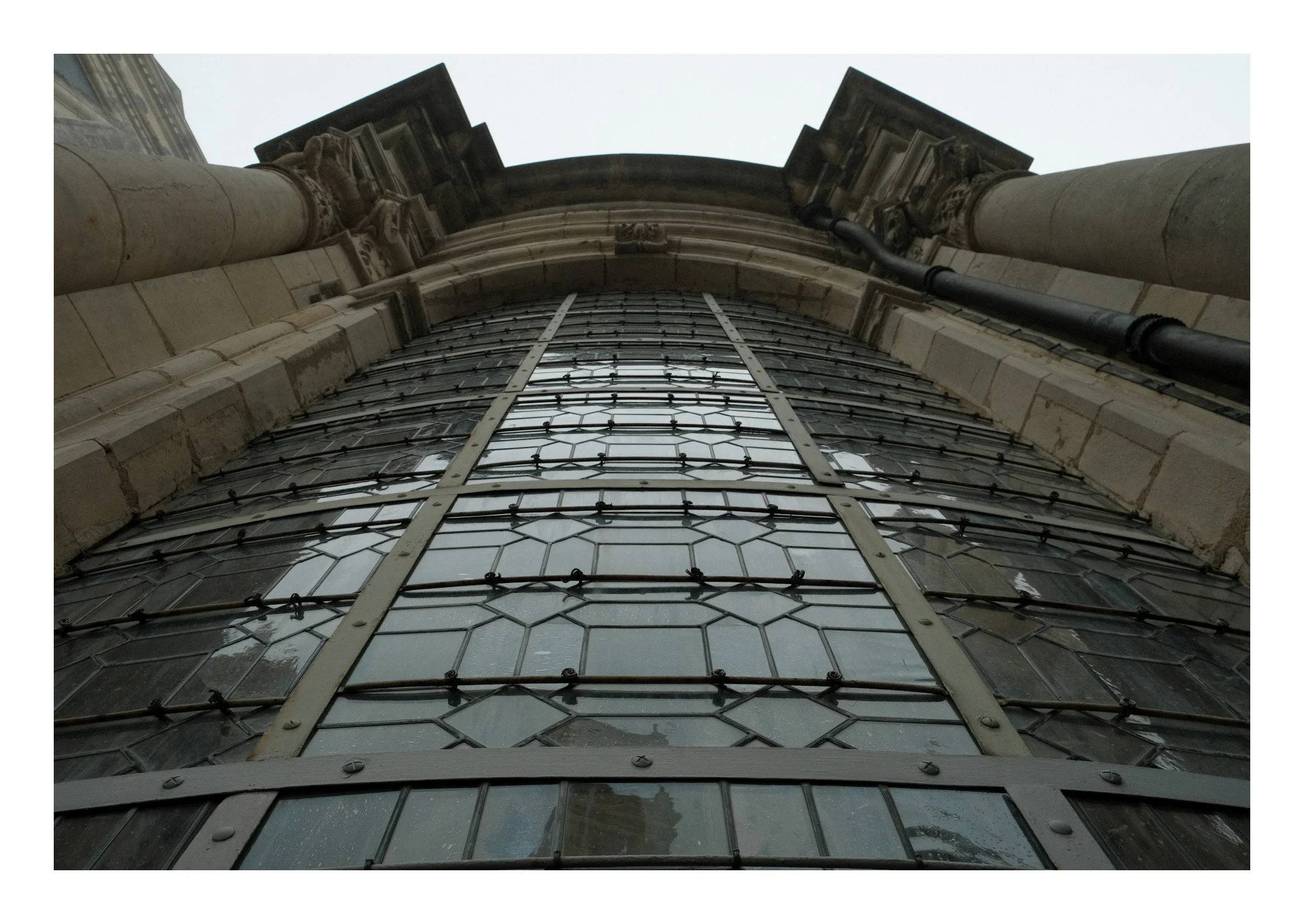 Low-angle view of a historic building's arched window with metal and glass panes, stone columns, and decorative architectural details.