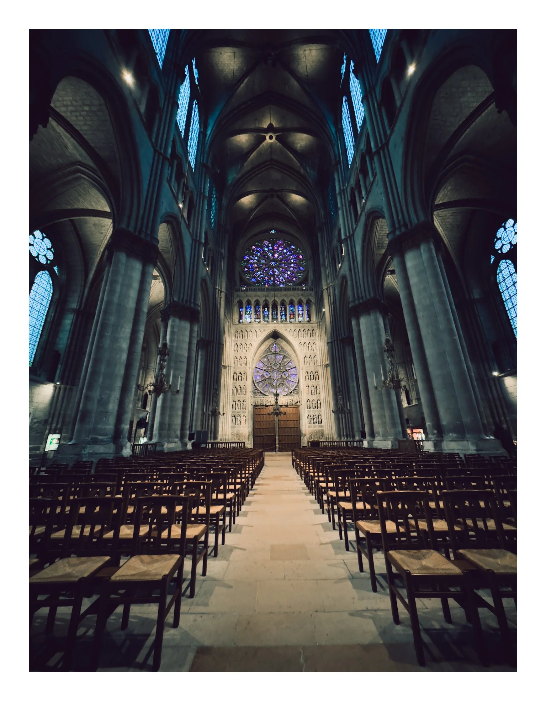 Interior of a Gothic cathedral with high vaulted ceilings, stained glass windows, and rows of wooden chairs leading to the altar.