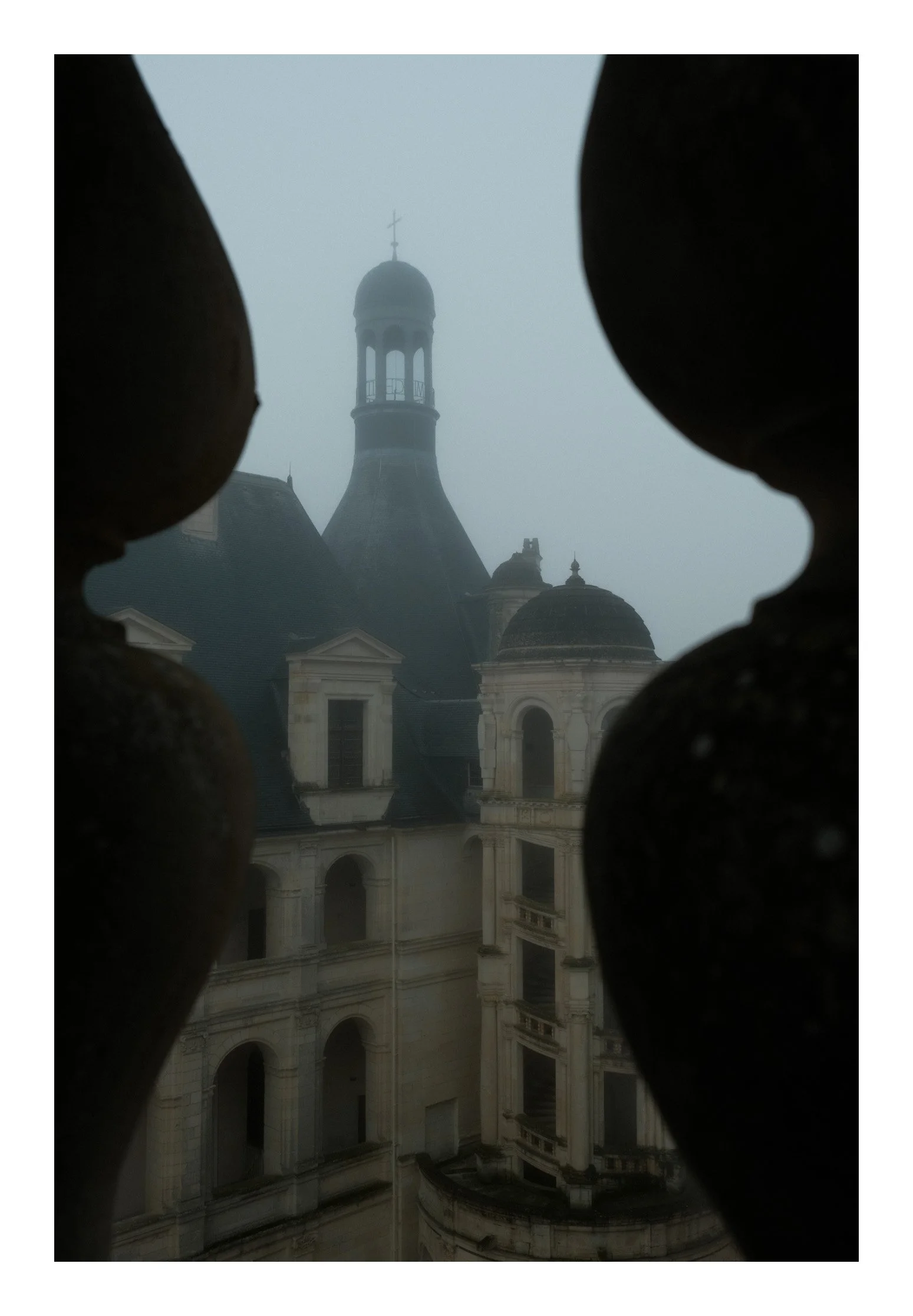 View of a historic church or cathedral with a tall bell tower, seen through a window framed by stone balustrades, on a foggy day.